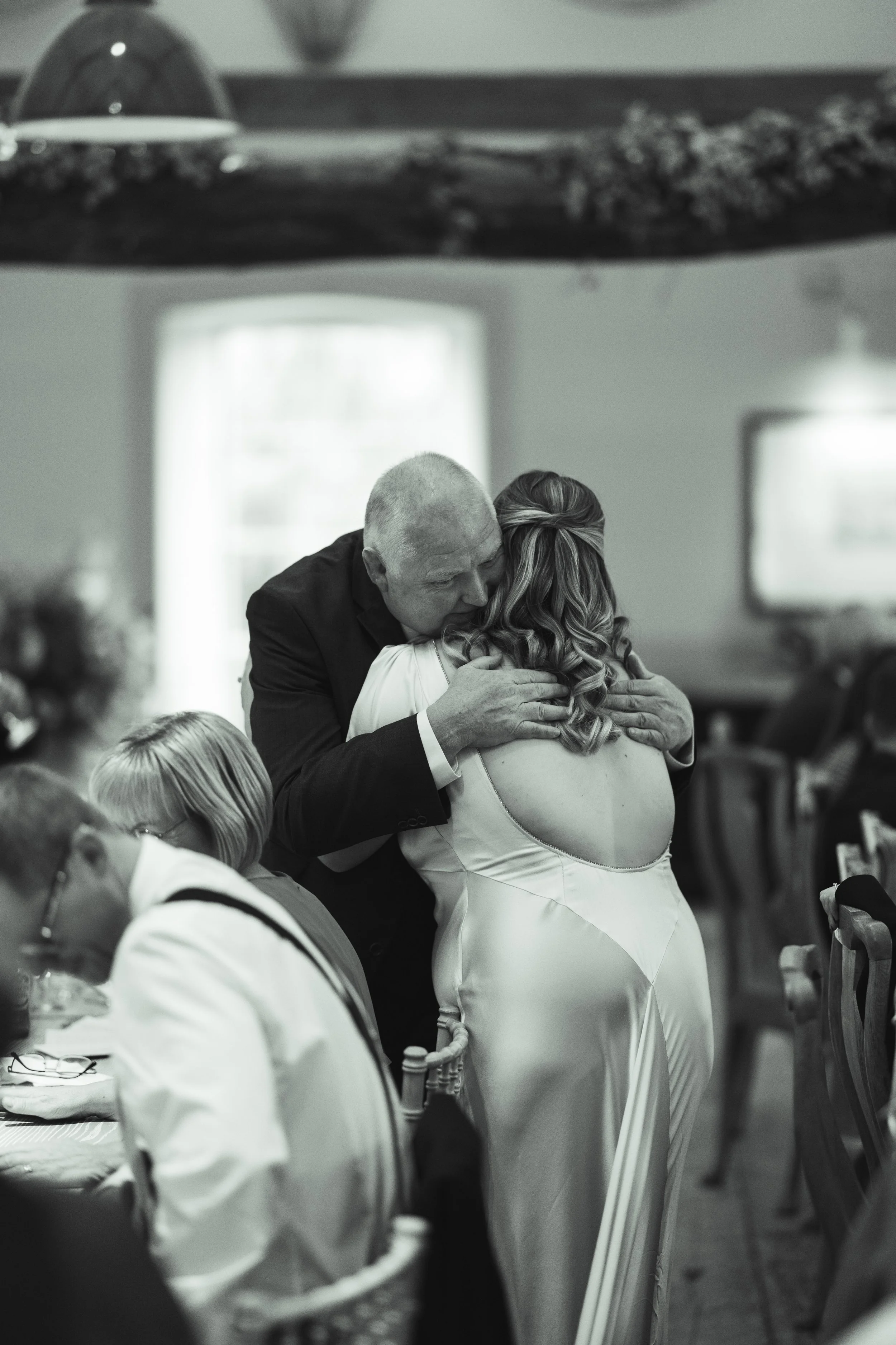 A man hugging a woman at a wedding reception in a decorated indoor venue.
