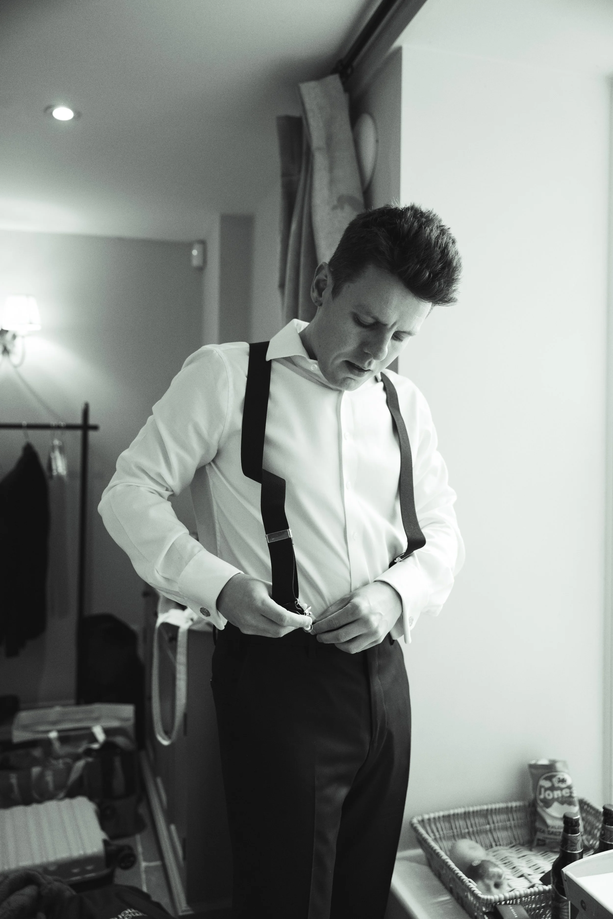 Man in formal attire putting on suspenders inside a room.