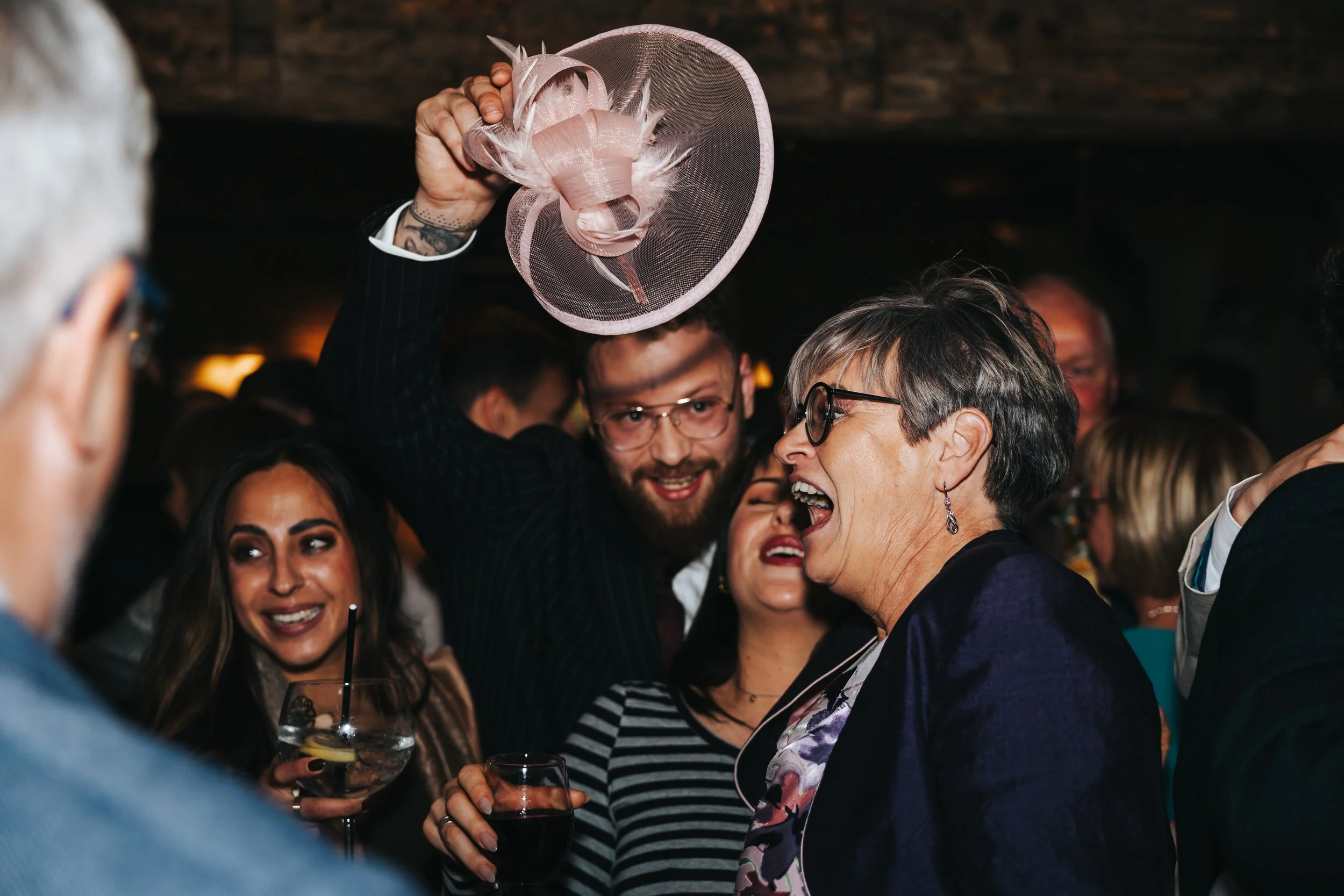 People dancing and celebrating at a party, with a woman holding a drink and a man holding a pink hat.