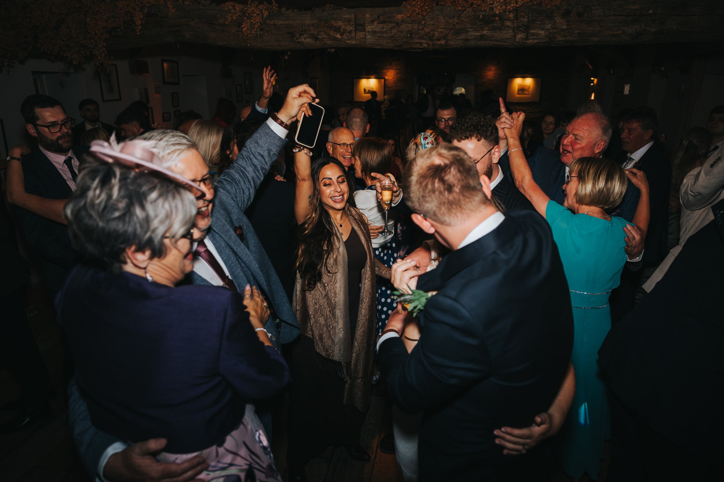 People dancing and celebrating at a lively indoor gathering or party, with joyful expressions and some holding drinks.