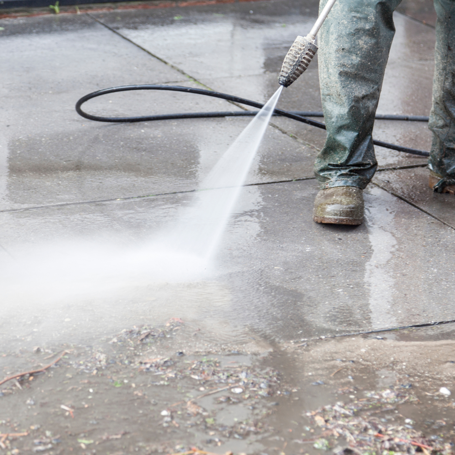 Person using a pressure washer to clean a wet concrete sidewalk.