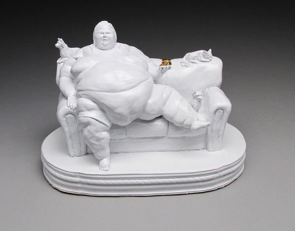 A white sculpture of a person sitting on a couch, with a cat on the armrest and a dog lying beside them, all on a round base.