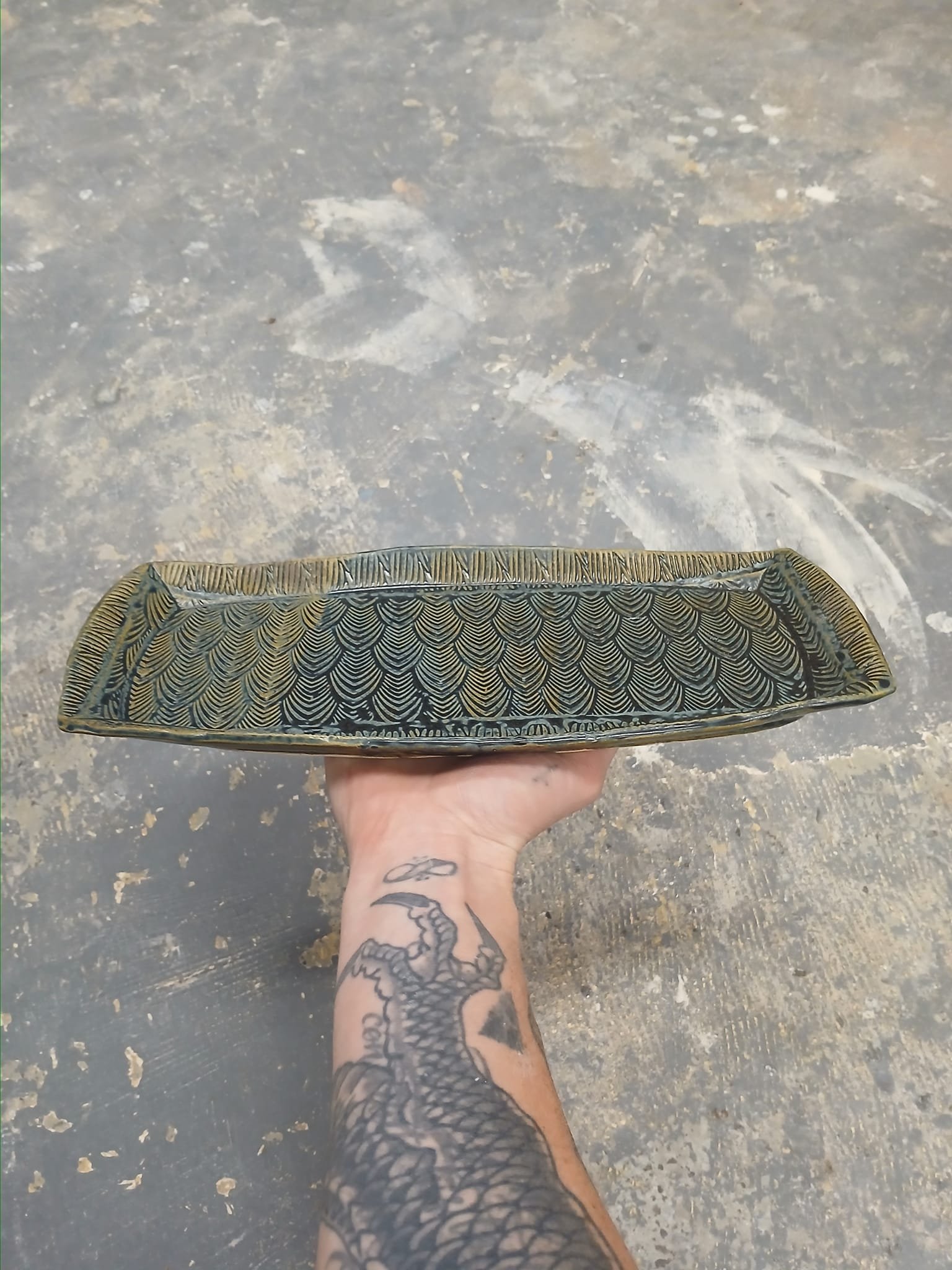 Hand holding a rectangular ceramic tray with intricate patterns against a textured background.