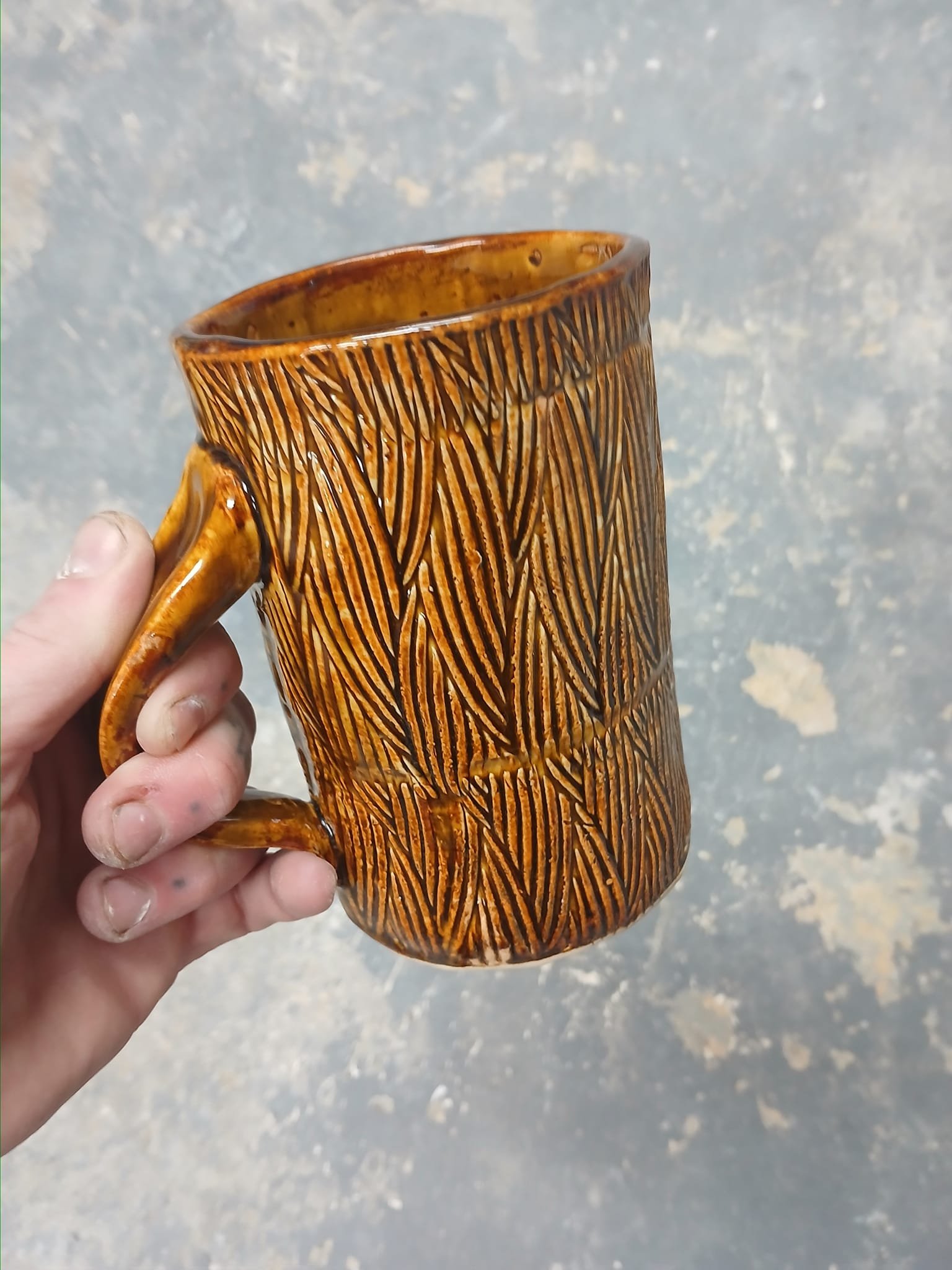 Hand holding a brown ceramic mug with a textured surface and leaf-like pattern.