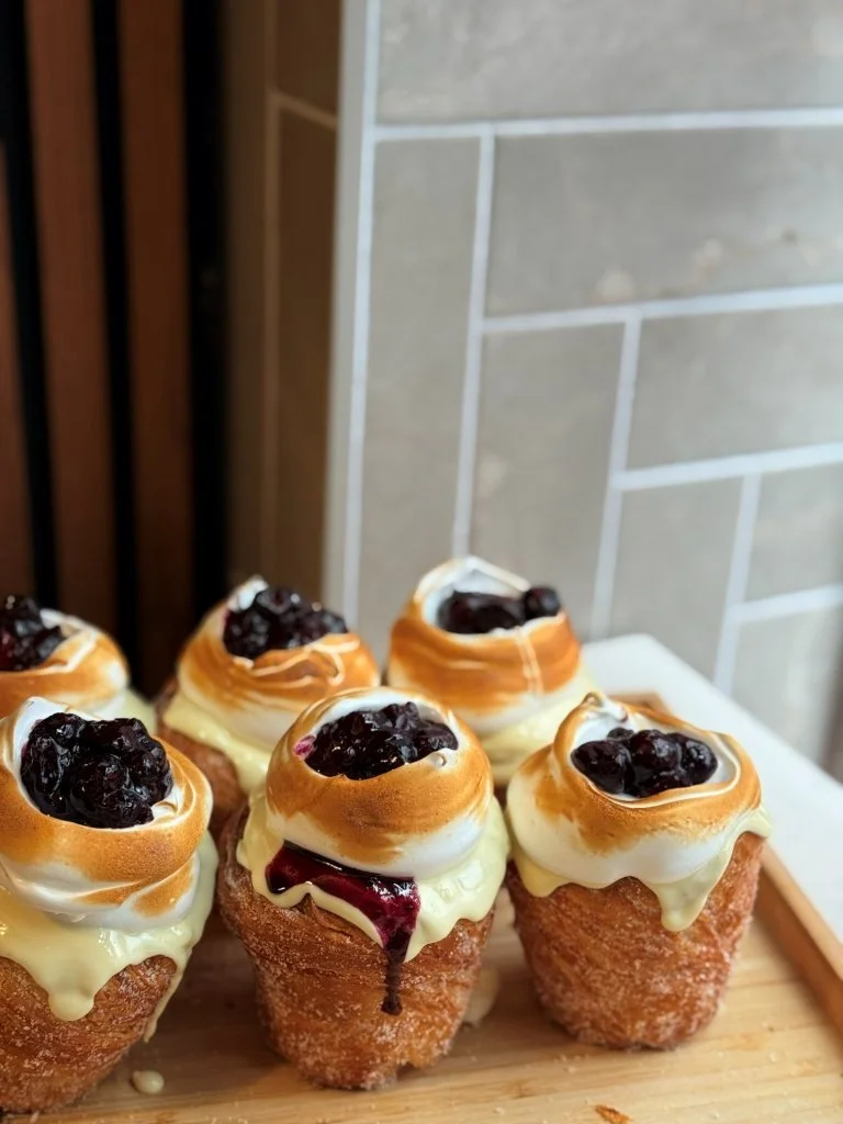 Six mini cheese cupcakes topped with blueberries and toasted marshmallow meringue on a wooden tray.