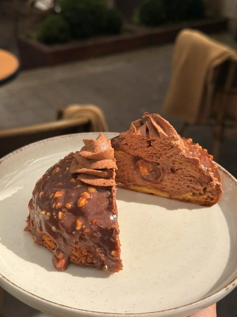 A plate with a chocolate dessert cut in half, topped with chocolate frosting or mousse, with a crunchy nut-covered exterior and a soft, layered interior.