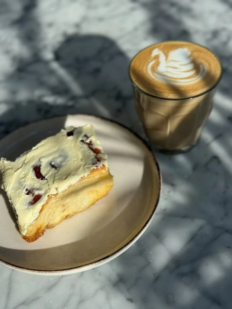 A slice of vanilla cheesecake with fruit topping served on a bowl, paired with a glass of iced coffee with whipped cream on top, placed on a marble surface.
