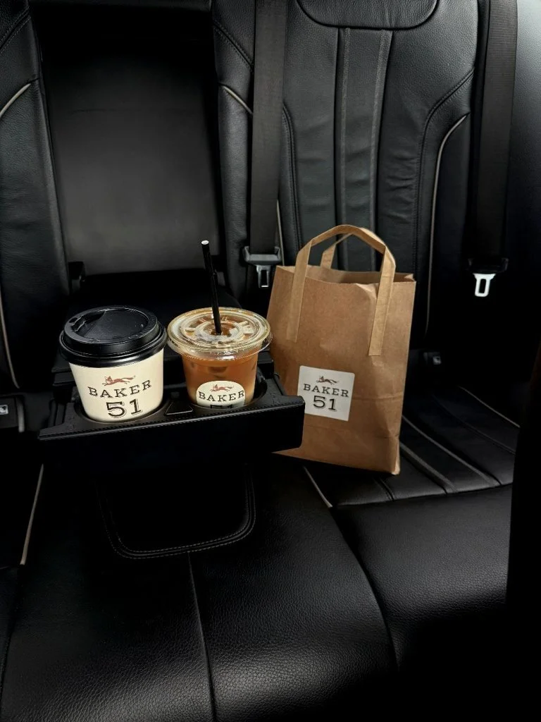 Coffee cups, a paper bag, and a beverage with a straw on a car's back seat.