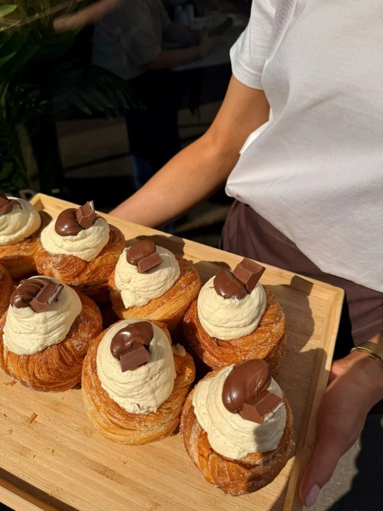 Several cream-filled pastry treats topped with chocolate pieces on a wooden tray.