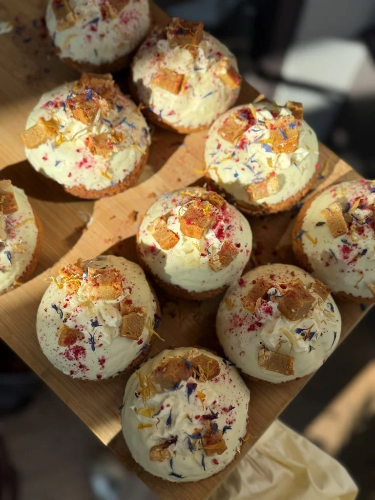 Cupcakes topped with white frosting, colorful sprinkles, small pieces of candy, and edible flowers.