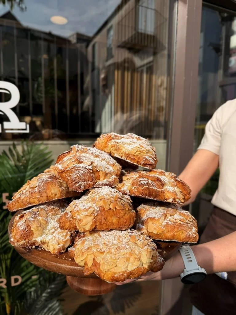 A person holding a plate of almond croissants outside a bakery or café.