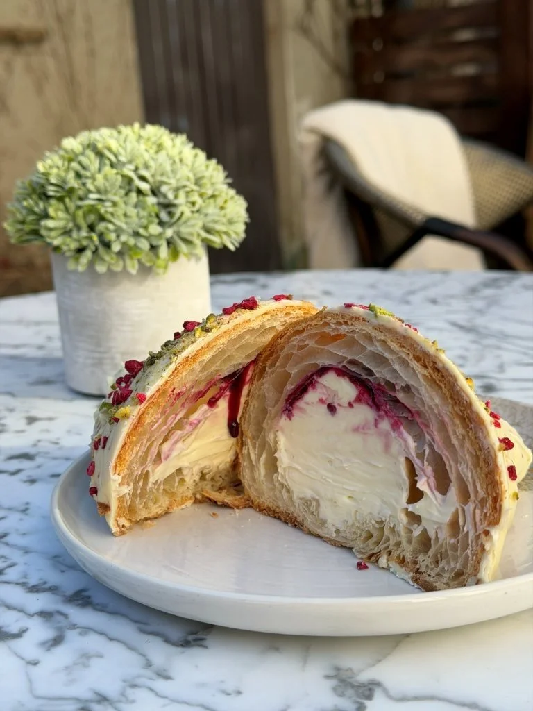 Cross-section of a cream-filled pastry cake with layers of flaky dough and decorated with red and green sprinkles, placed on a white plate on a marble table outdoors.