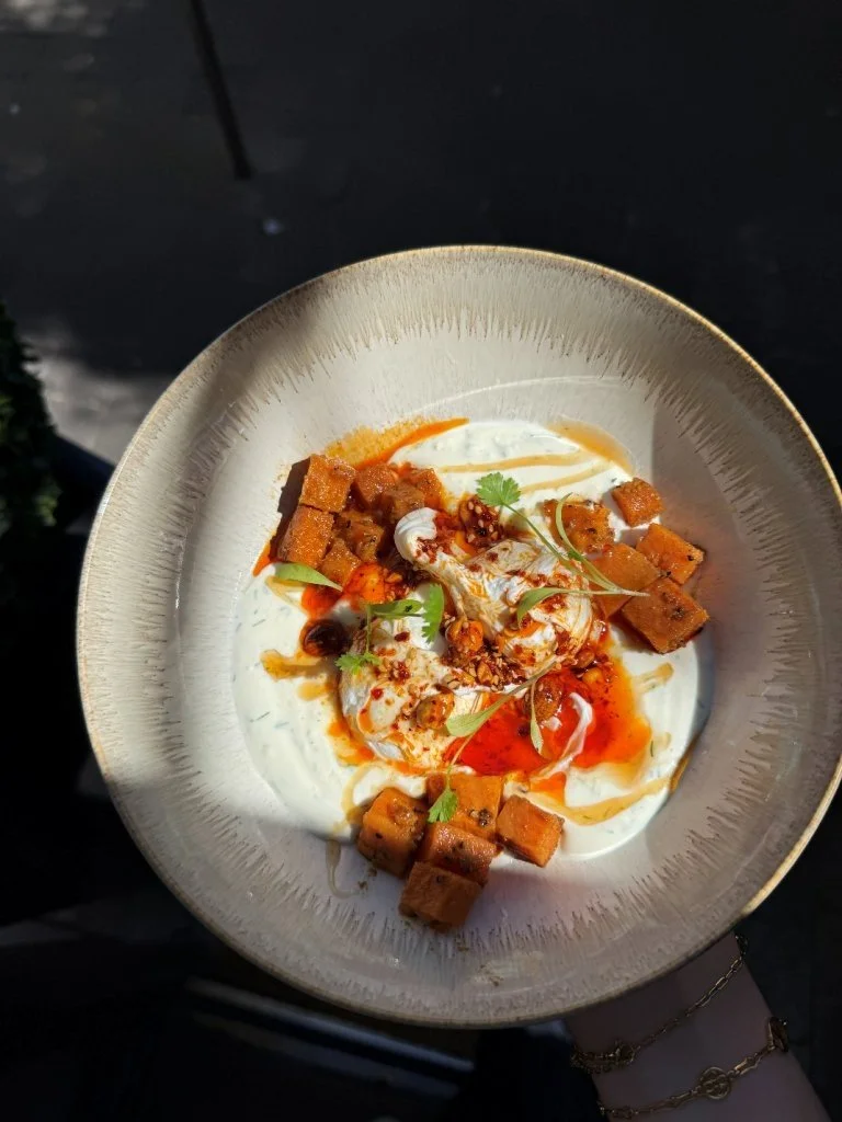 A bowl of creamy yogurt topped with crispy fried tofu, chili oil, fresh cilantro, and spices.