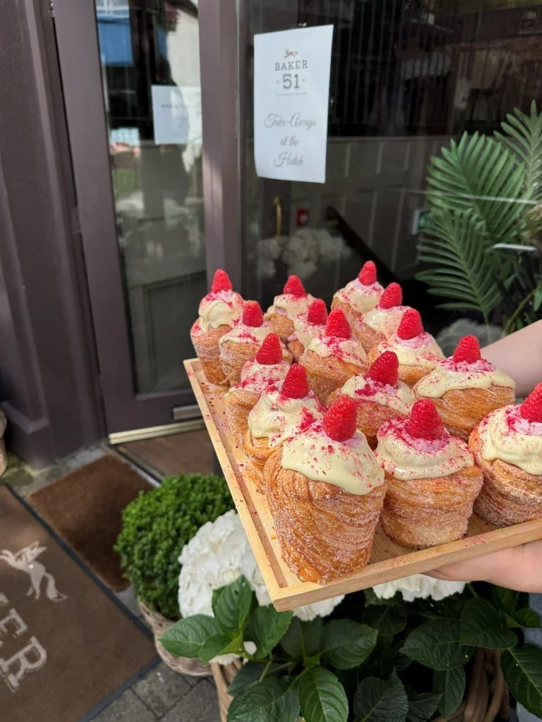 Tray of cream-filled pastries topped with raspberries, held outside a bakery.