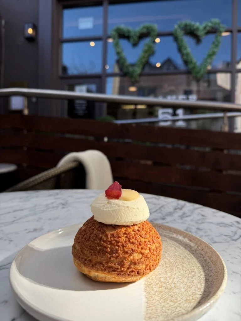 Cream-filled pastry topped with icing, a small piece of raspberry, and a drizzle of white chocolate, served on a white ceramic plate with a marble table background.