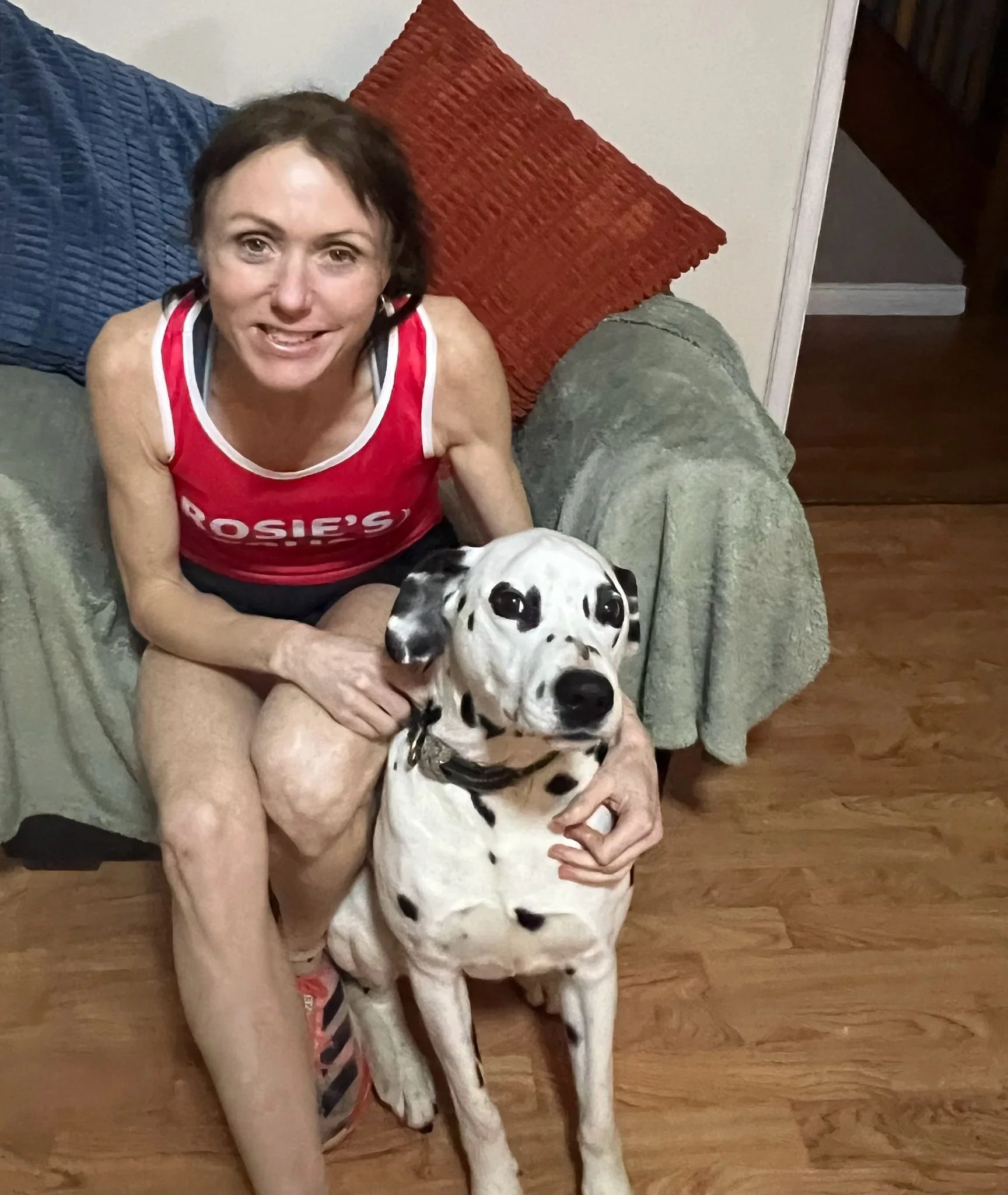 woman sitting beside dalmatian wearing Rosie's Trust running vest indoors 