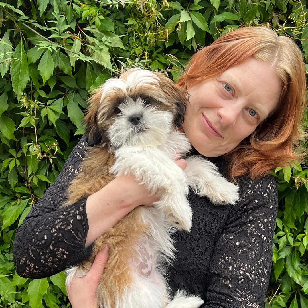 Woman holding a fluffy puppy in front of green leaves.