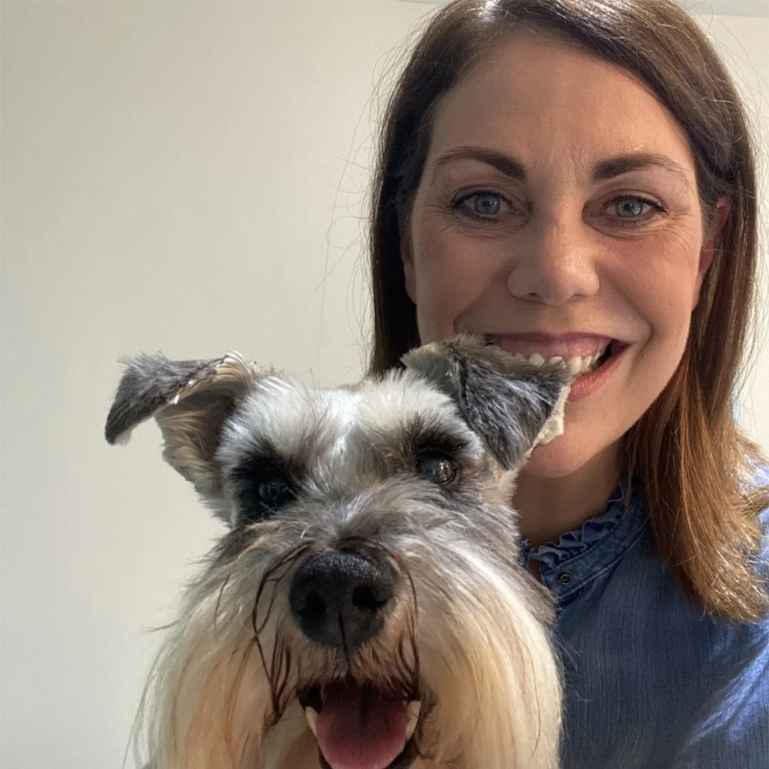 Woman smiling with a gray and white Schnauzer dog in a selfie.
