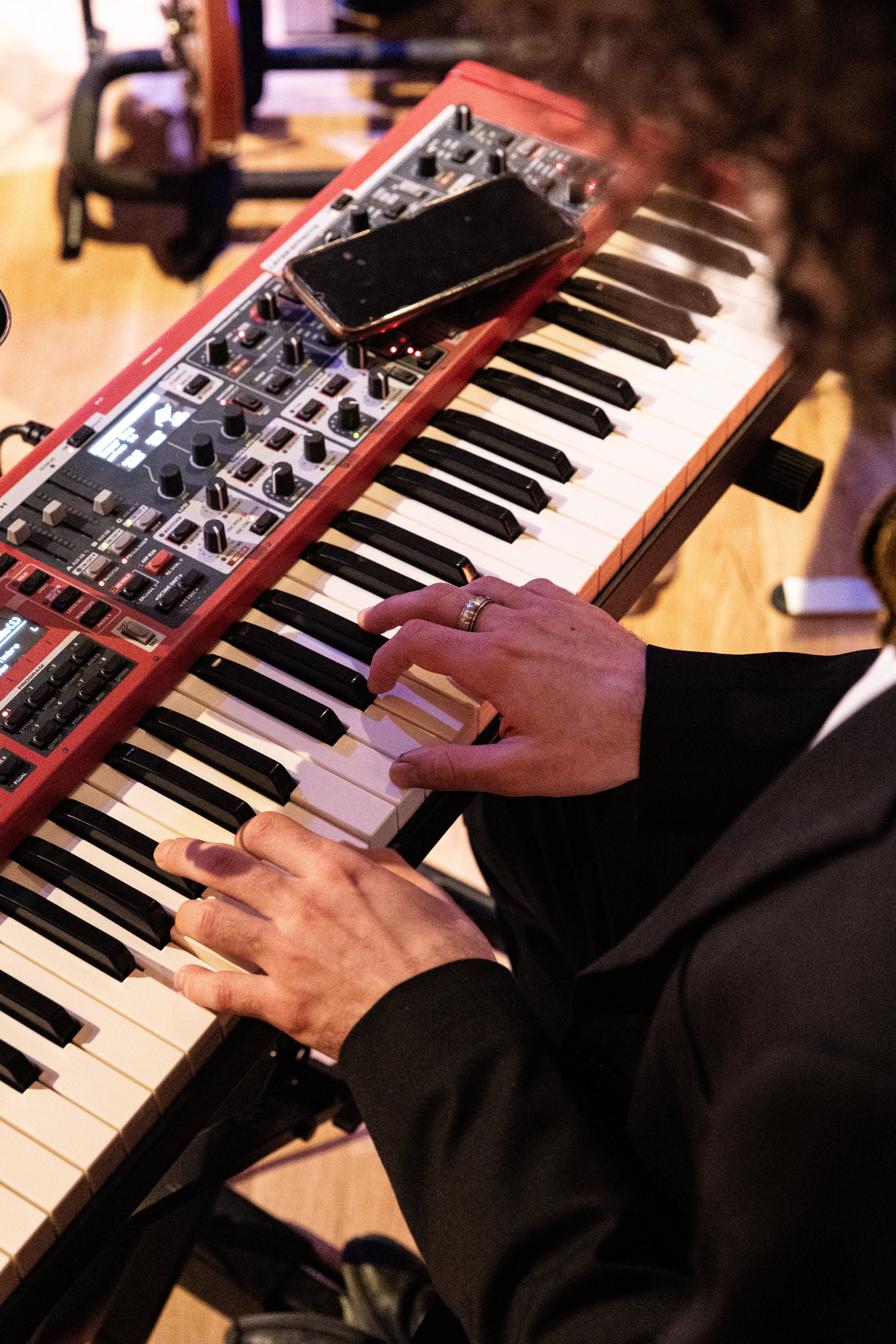 Eine Person spielt auf einem roten elektronischen Keyboard, auf dem ein Smartphone liegt, während sie mit den Händen die Tasten drückt.