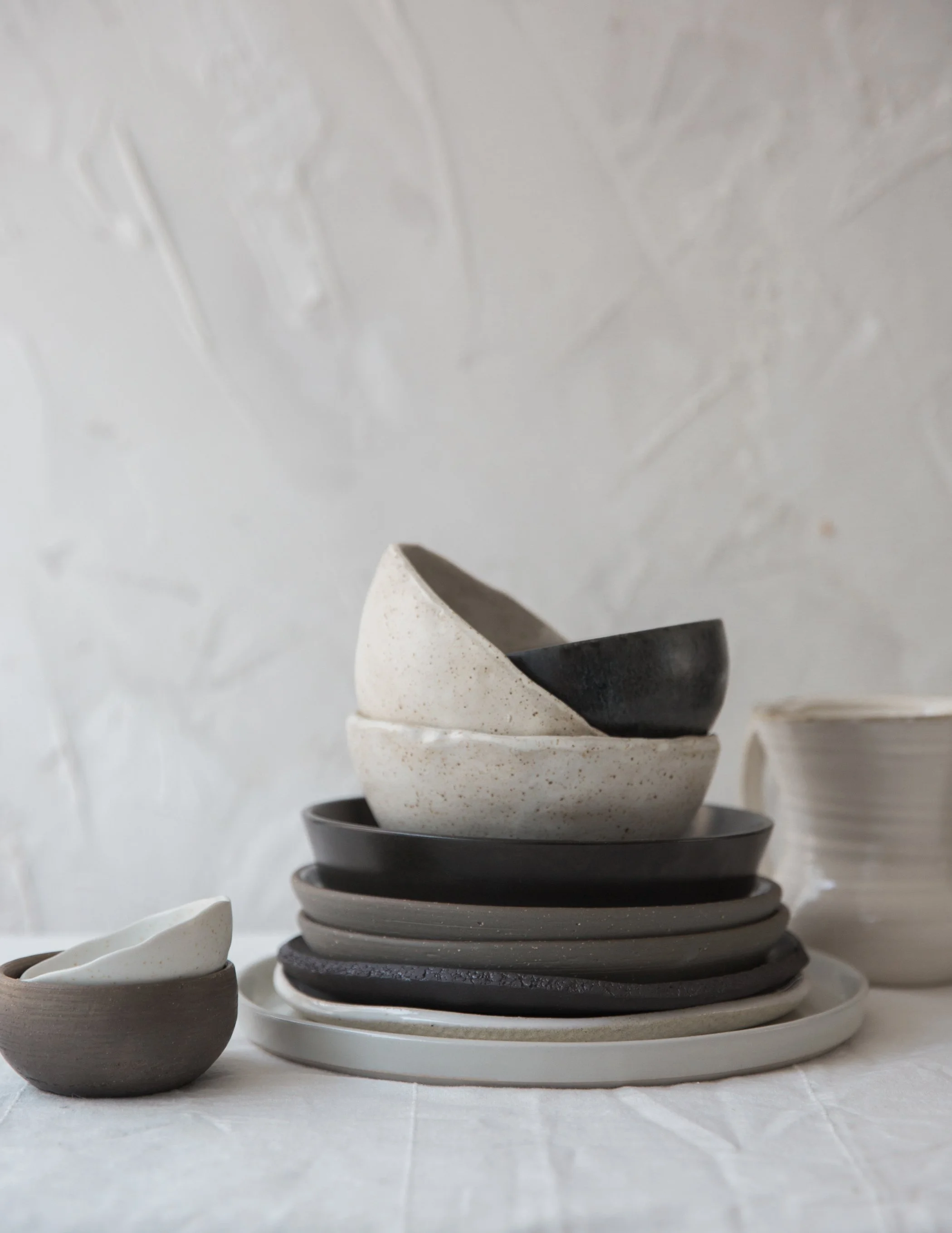 Stacked handmade ceramic bowls in cream and charcoal tones against a textured plaster wall