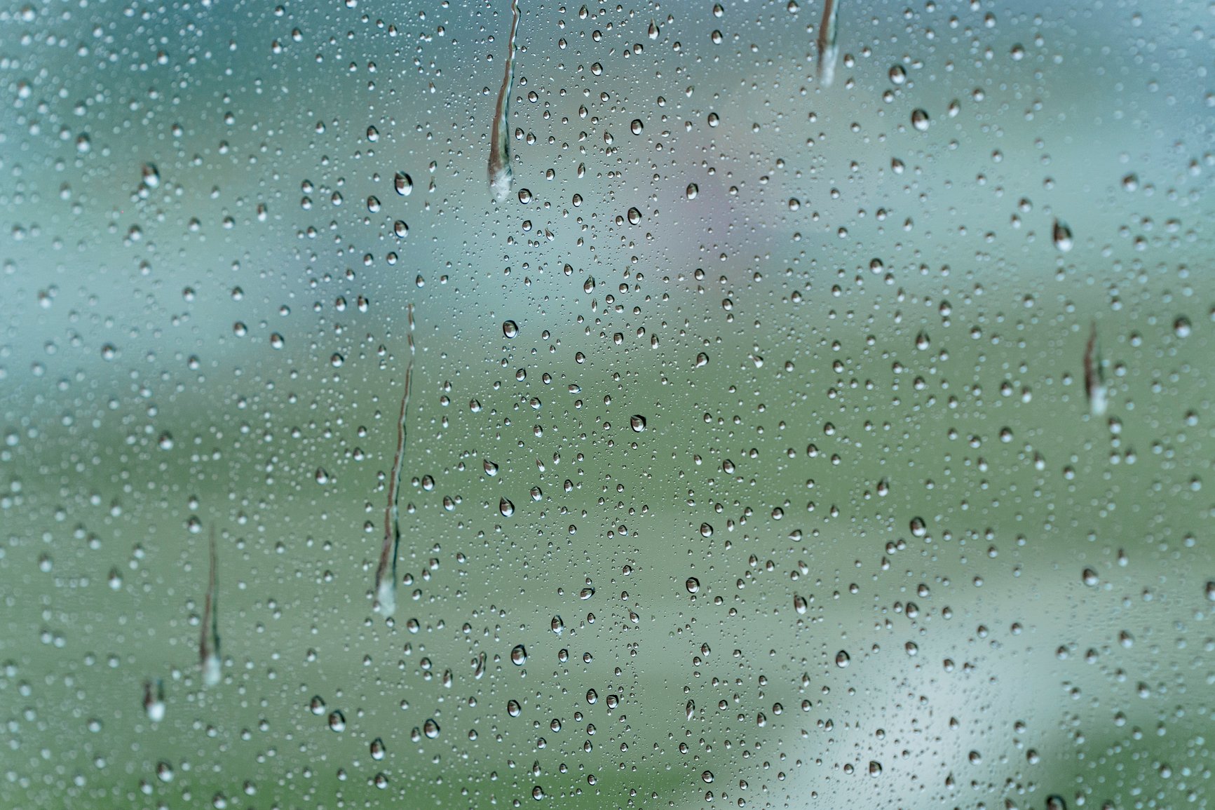 Raindrops streaking down a window with soft green light behind