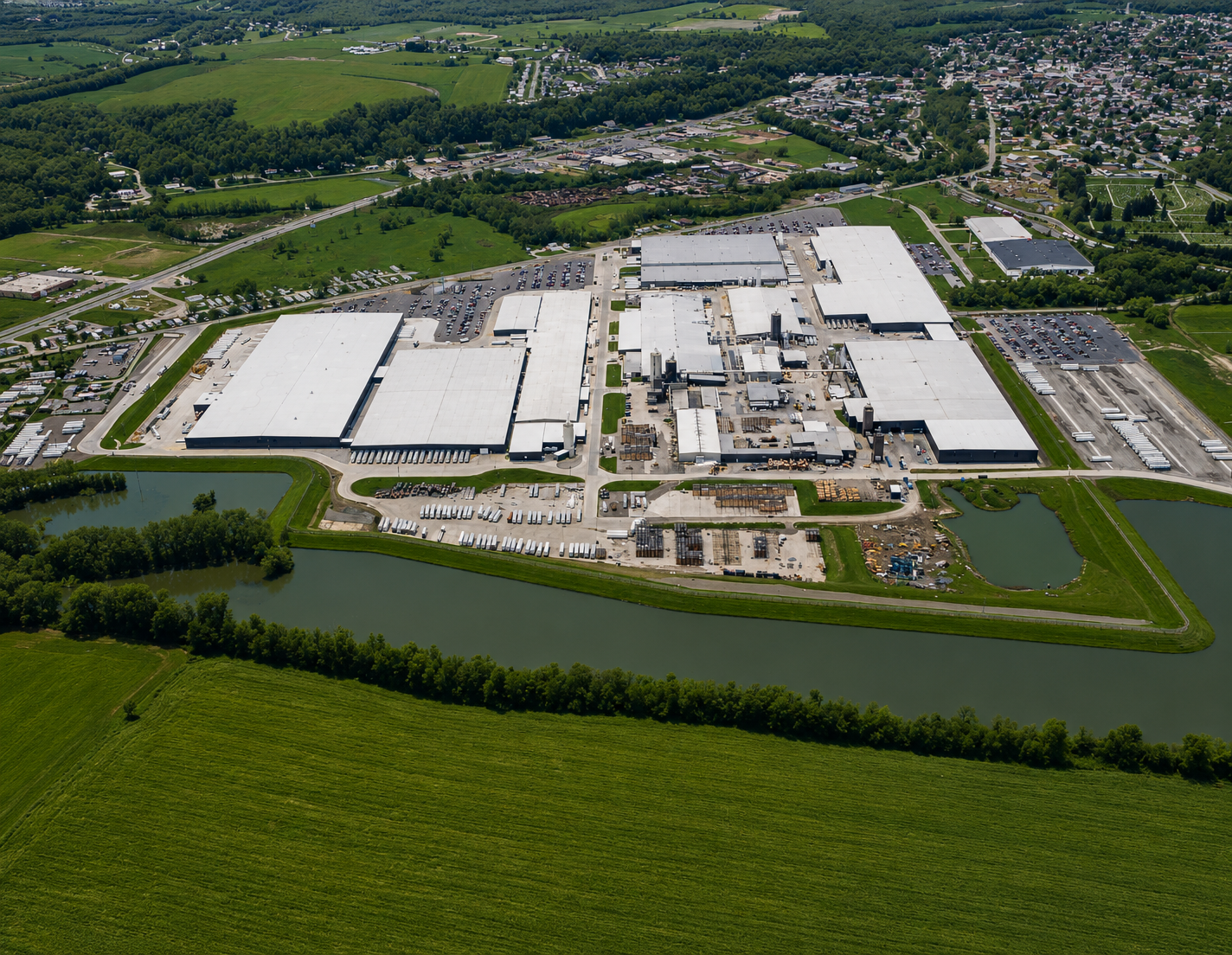 Aerial view of an industrial complex surrounded by water, greenery, and a nearby residential area.
