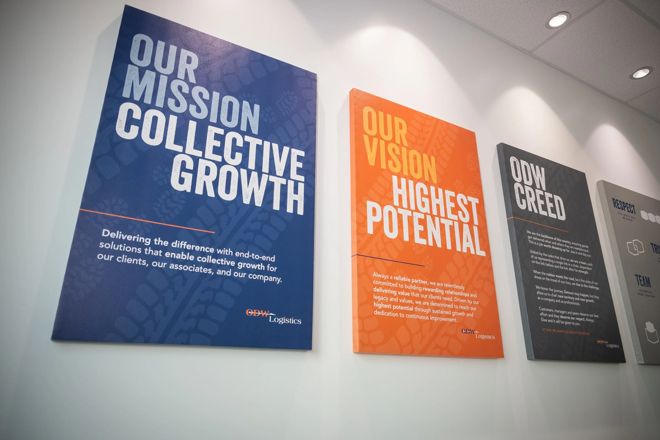 Three banners on a wall displaying company mission, vision, and values. The first banner reads 'Our Mission: Collective Growth,' the second 'Our Vision: Highest Potential,' and the third 'Our Creed: Respect, Trust, Team,' each with descriptive text at the bottom.