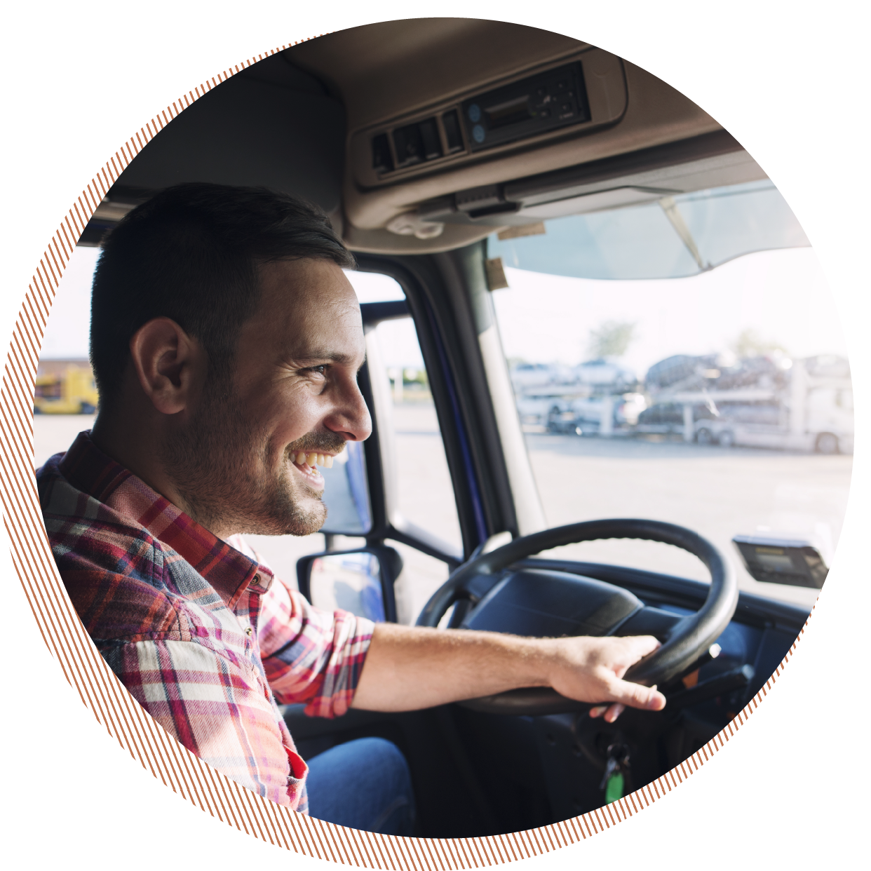 A man smiling and driving a truck, with a view of a parking lot with multiple vehicles through the windshield.