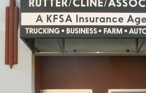 Close-up of a business sign with the text 'RUTTER/CLINE/ASSOC', indicating it is an insurance agency, and smaller text listing services like trucking, business, farm, and auto.
