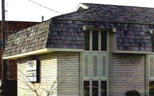 A two-story house with a brick exterior, a shingled roof, and tall narrow windows on the front.