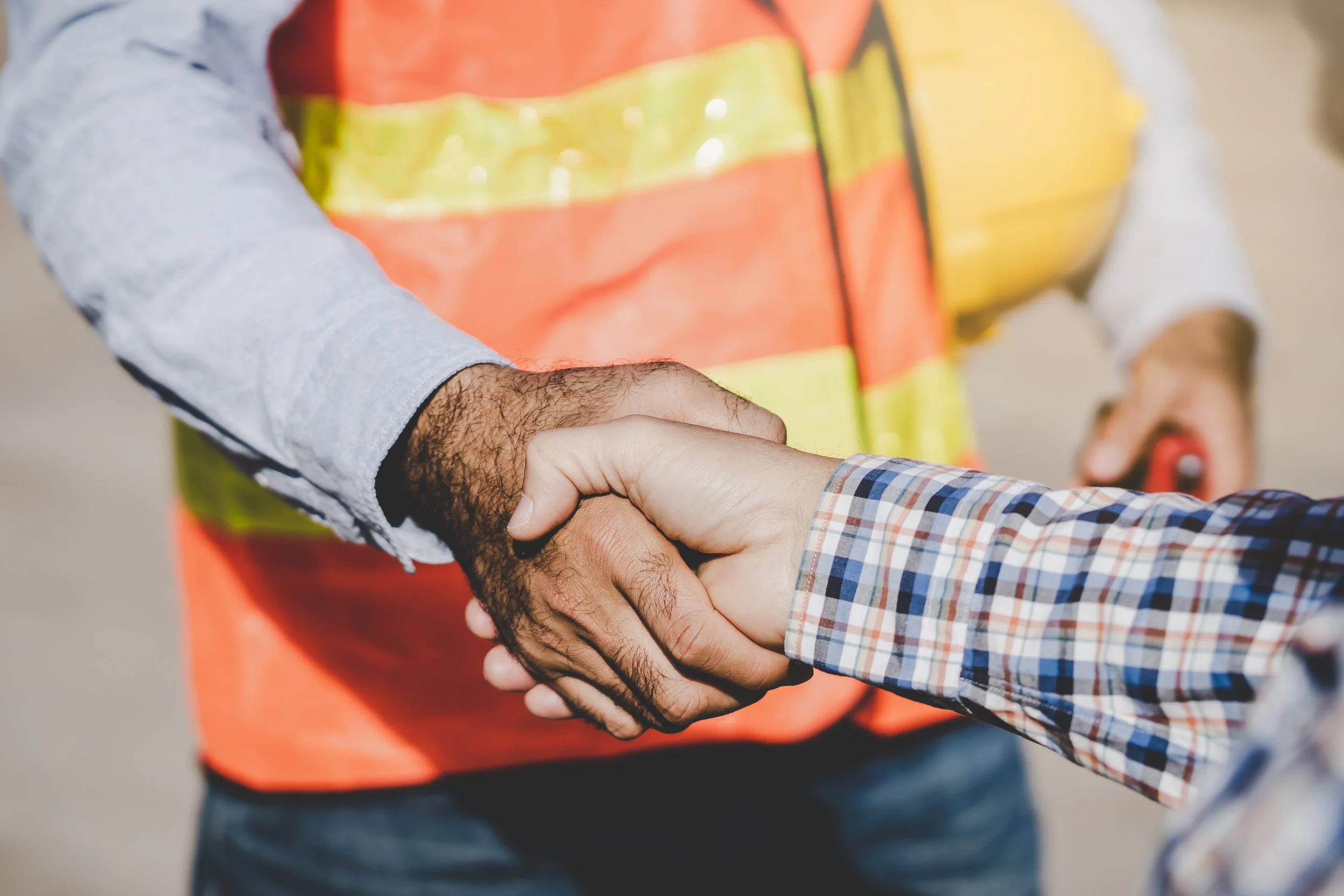 A person wearing a high-visibility safety vest shaking hands with another person wearing a checkered shirt.