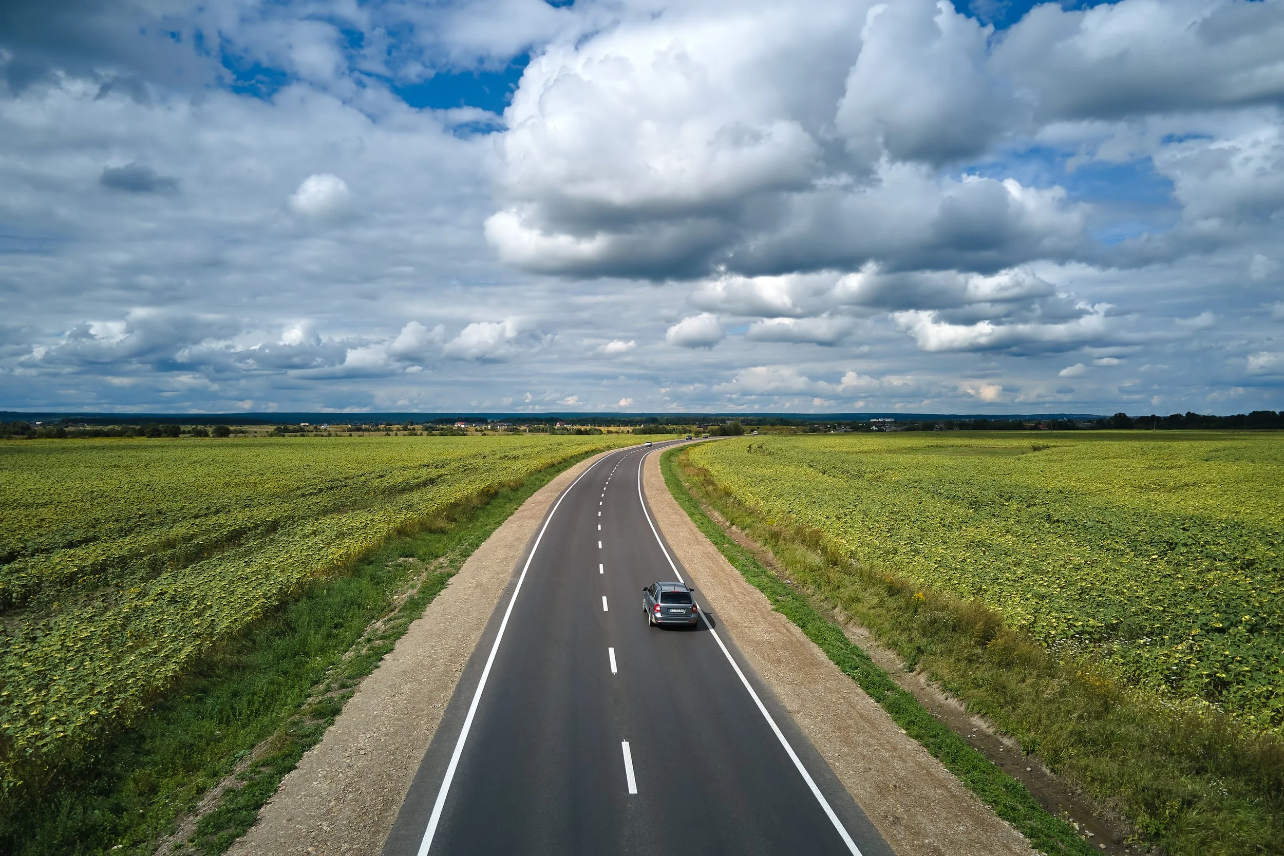 A two-lane road running through green farmland under a partly cloudy sky.