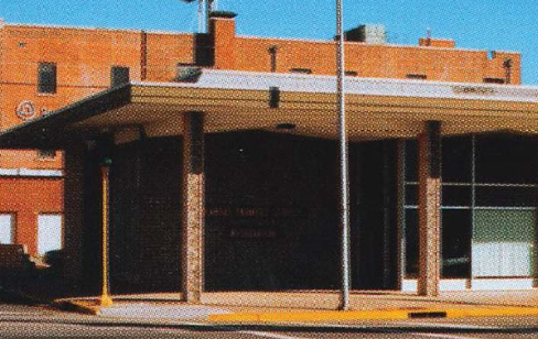 A brick building with a flat overhang entrance supported by columns and a flagpole in front.