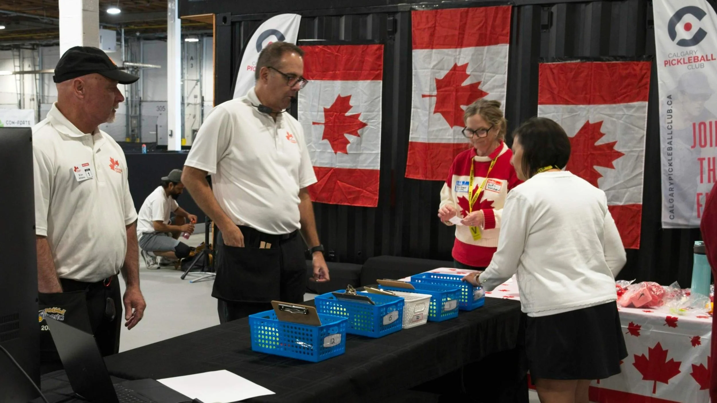 Group of people at a booth decorated with Canadian flags at an event, with items on tables and banners in the background.