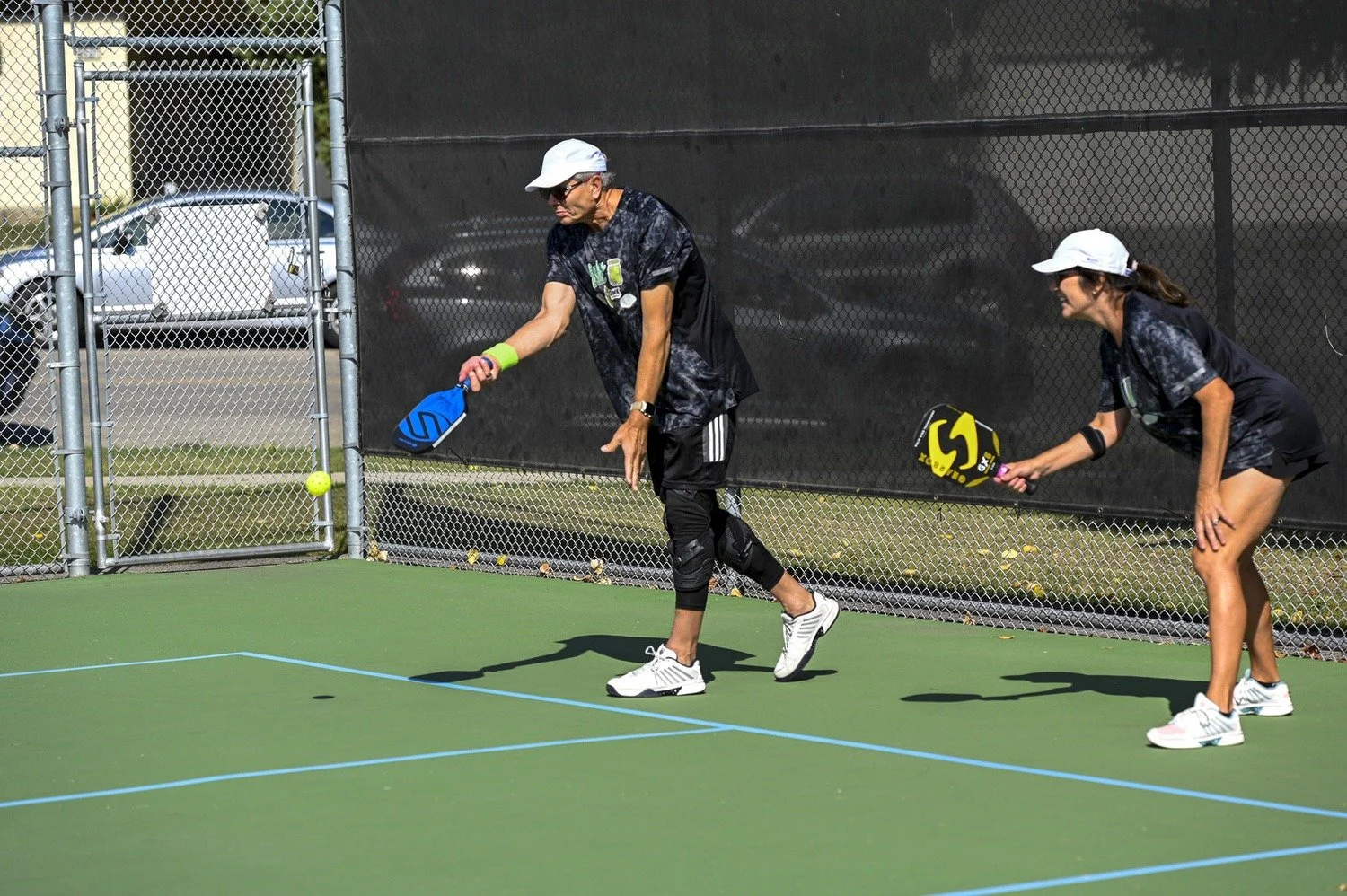 Two women playing pickleball on an outdoor court, preparing to hit a ball with paddles.