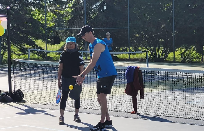 A young girl and a coach on a tennis court, with the coach giving instructions as they hold tennis rackets during a sunny day.