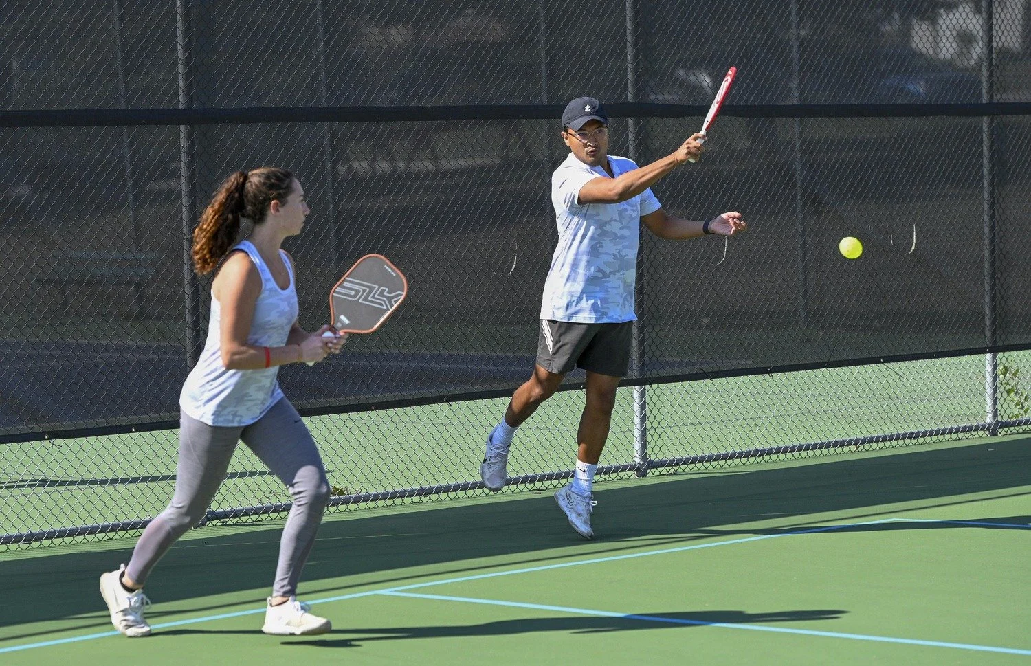 Two people playing pickleball on an outdoor court, one is hitting a ball while the other prepares to hit it back.