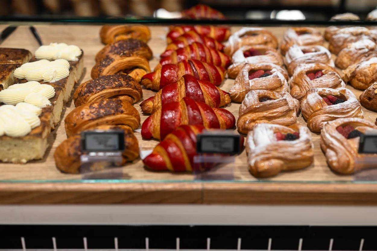 Assorted bakery pastries including croissants, fruit Danish pastries, and other sweet baked goods on display at a bakery.