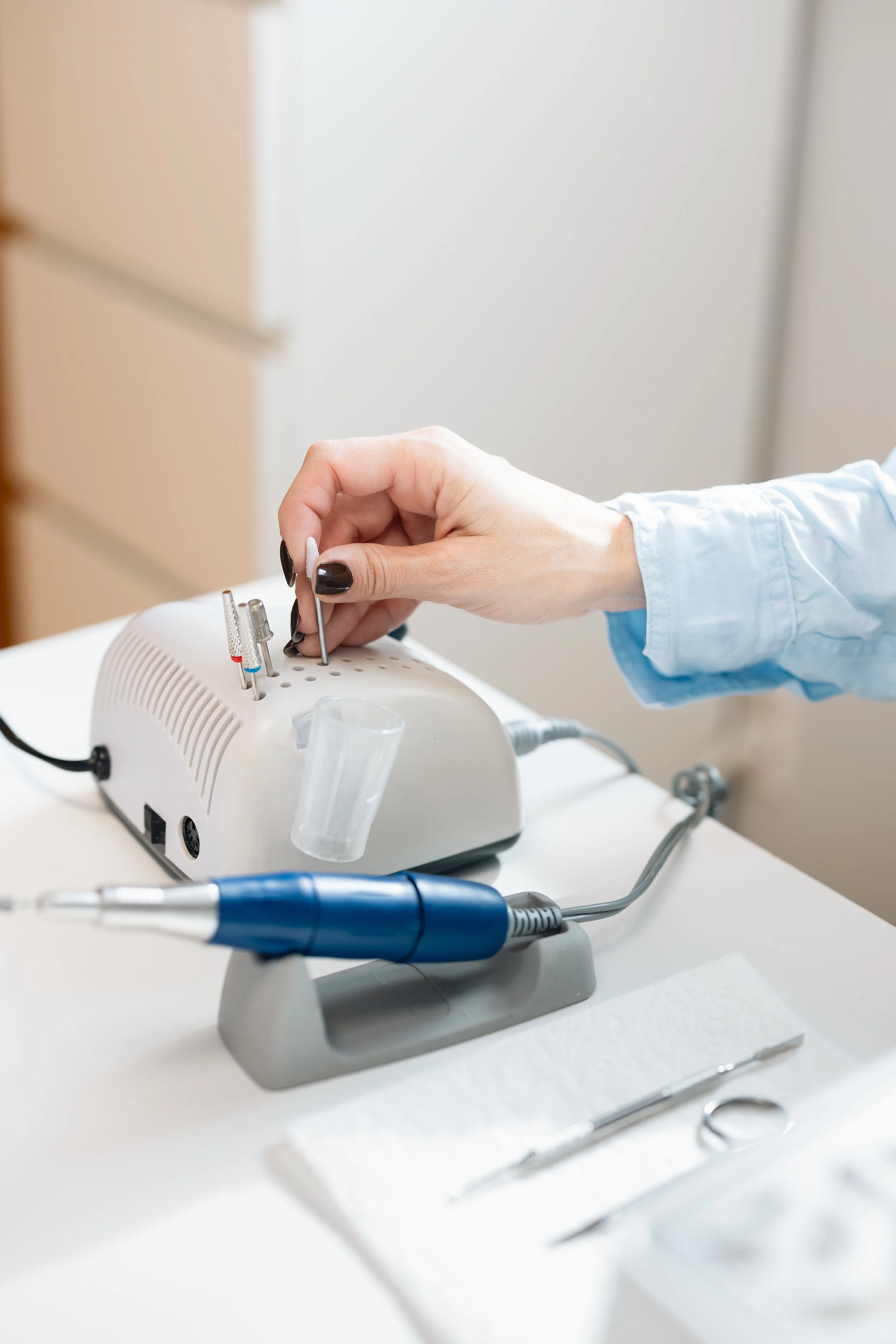 A person using a pedicure drill machine at a nail salon, with various manicure tools on a white cloth.