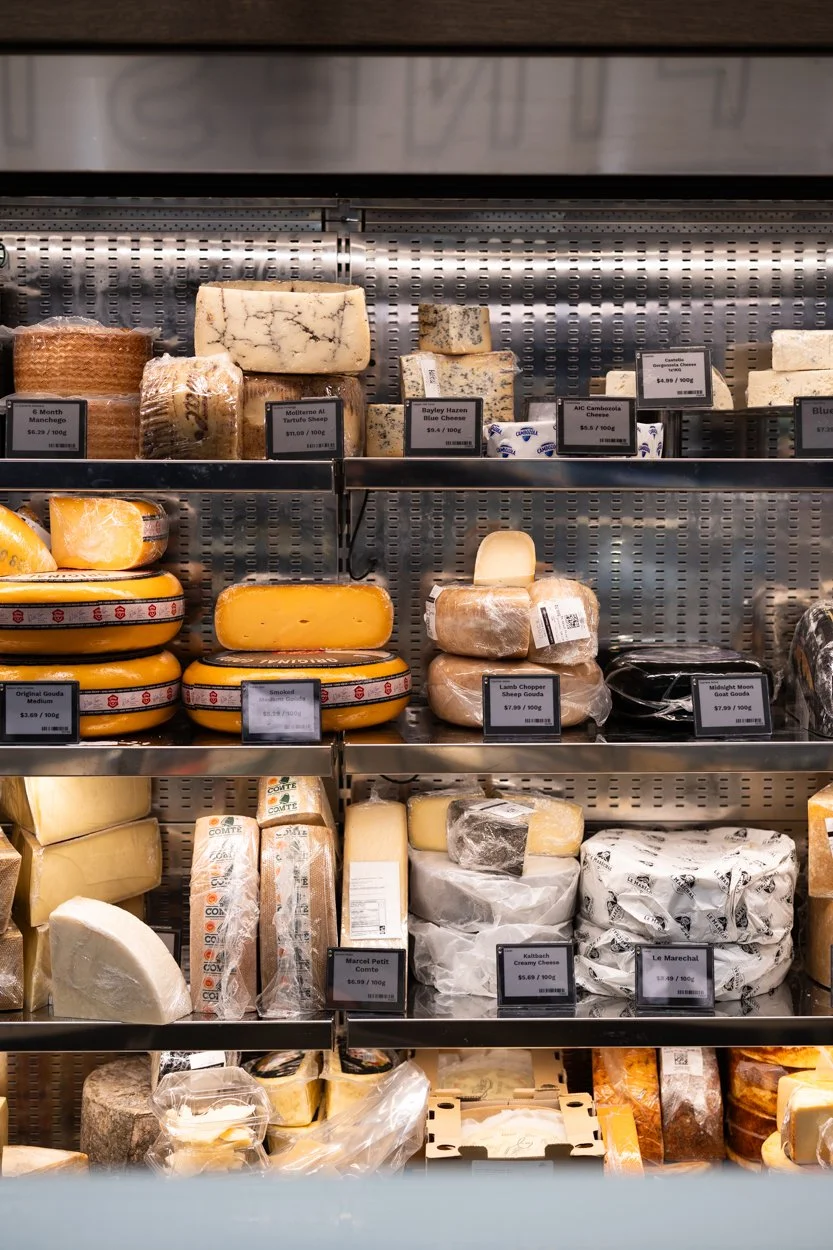 A cheese display case with various types of cheese, including blue cheese, gouda, and sheep cheese, with price tags and labels.