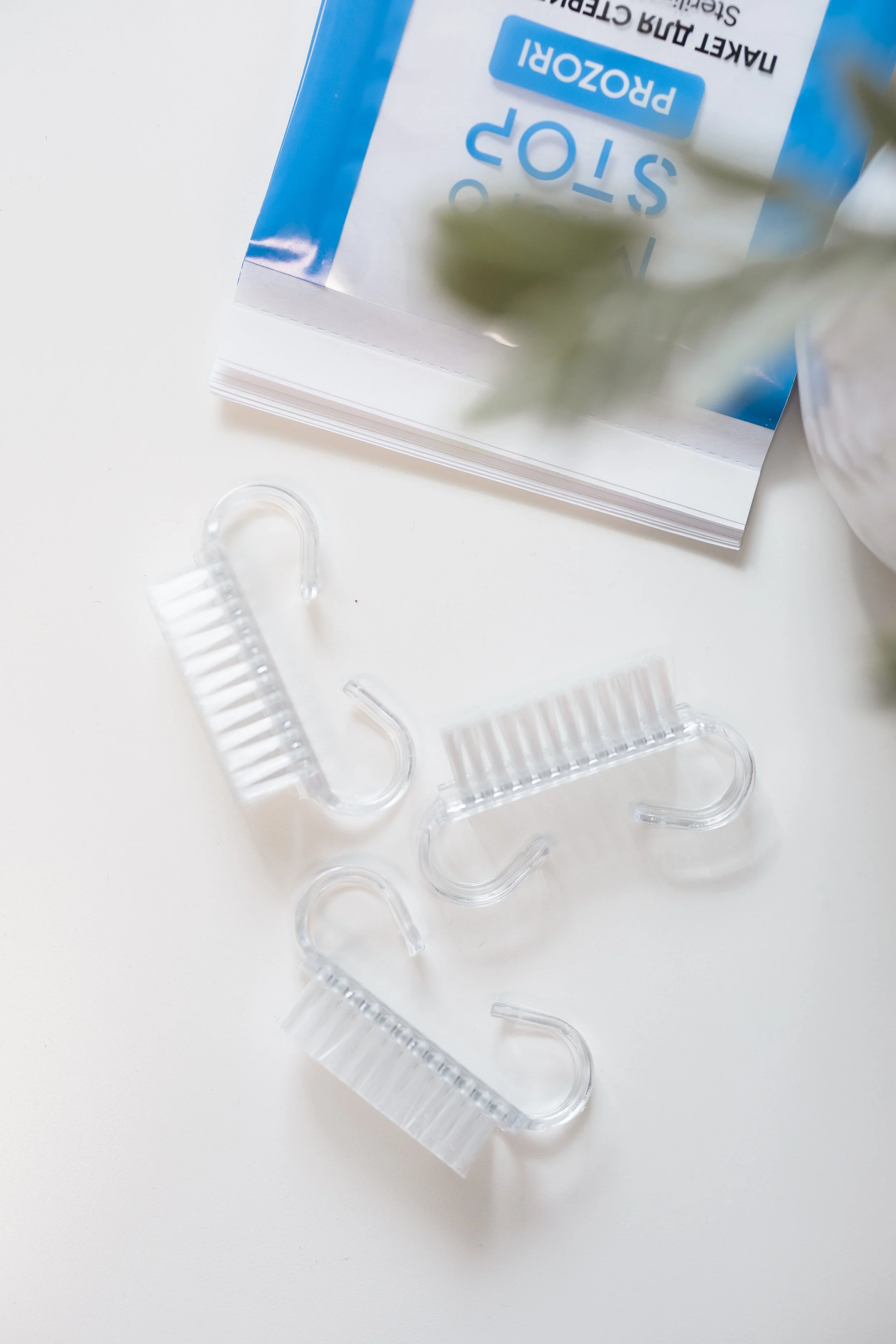 A white surface with four clear plastic eyelash curlers and a partially visible box of PROZOR 50+ sun protection cream.