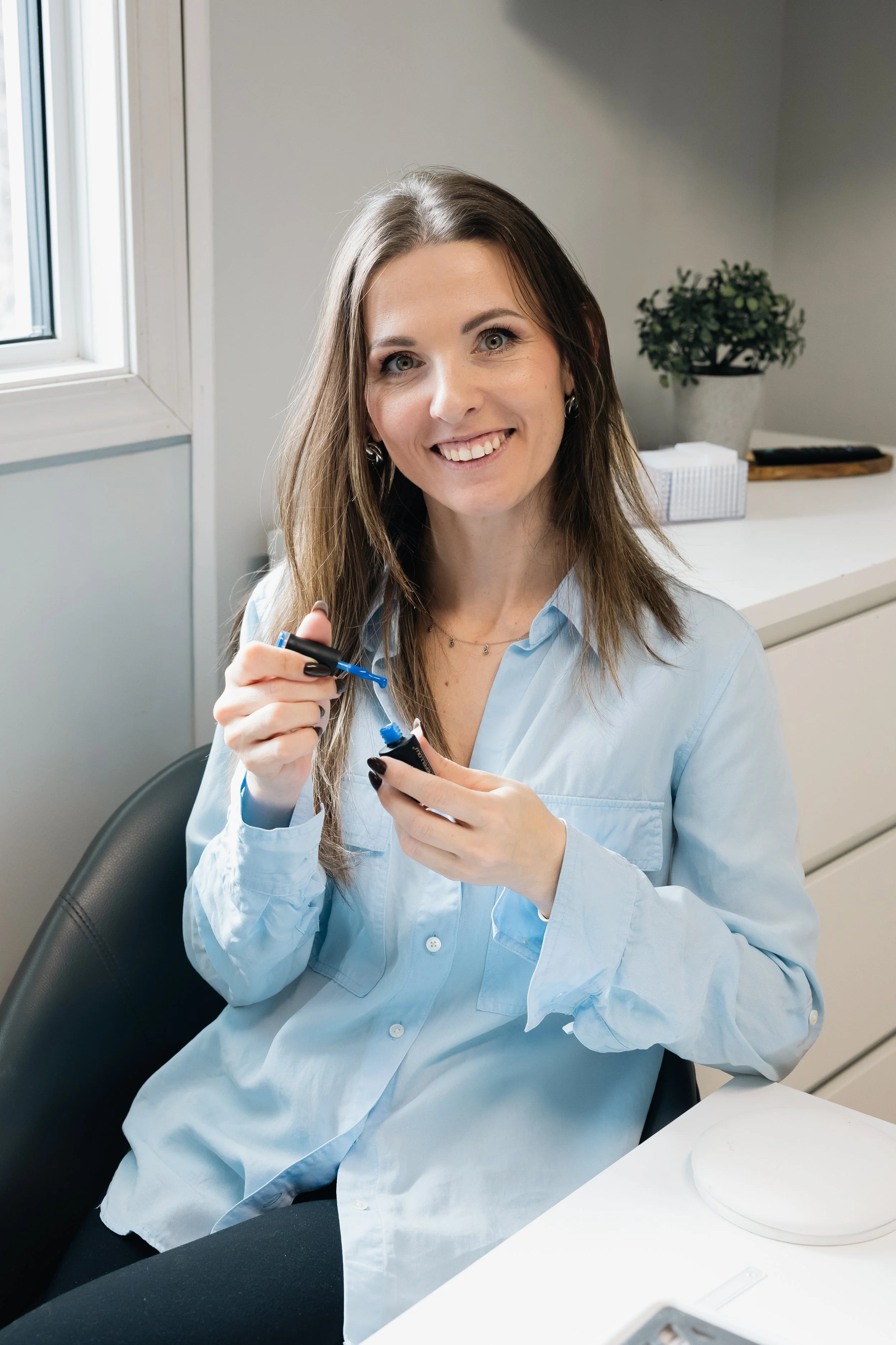 Woman in light blue shirt applying nail polish at a desk