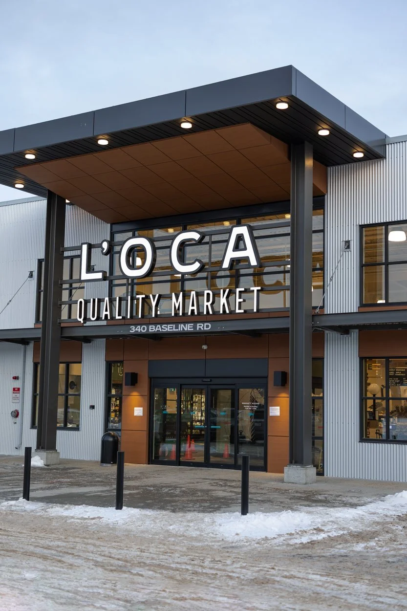 Exterior view of L'OCA Quality Market, a modern grocery store at 340 Baseline Road, with snow on the ground and a cloudy sky.