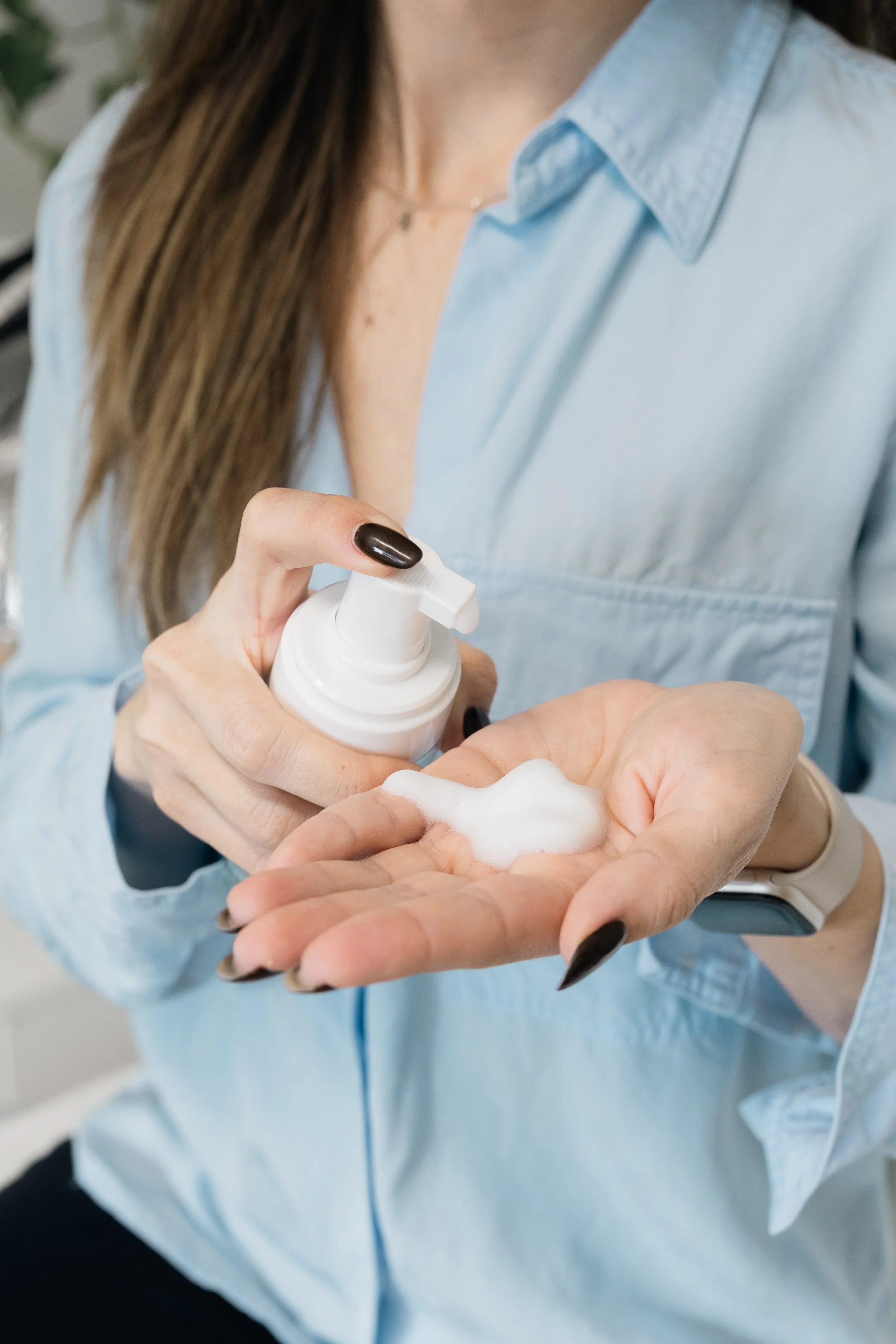 A person in a light blue shirt pumps white foam from a bottle into their hand.