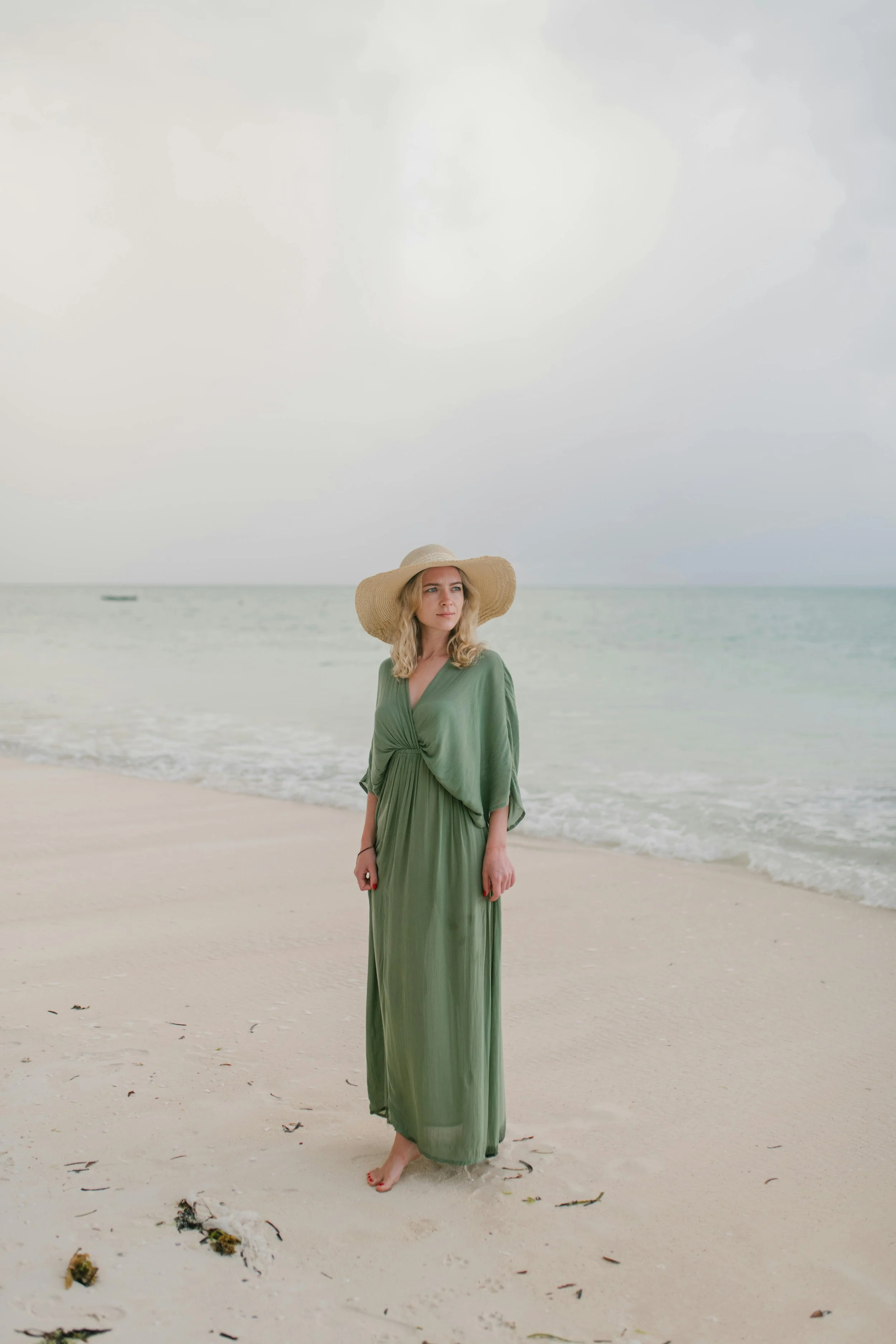 Woman in a green dress and sunhat standing on the beach