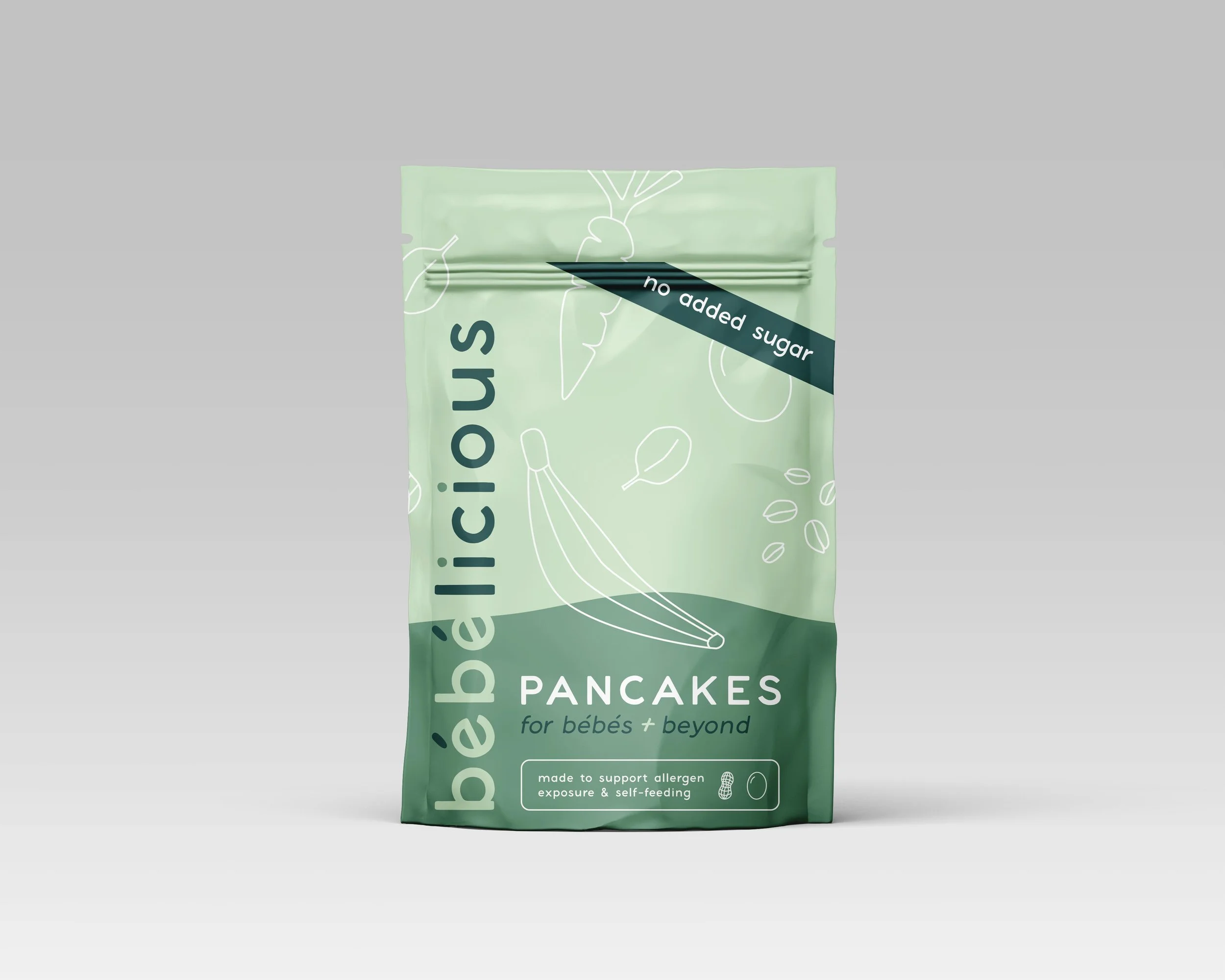 Light green package of béilélicious pancakes for babies and beyond with a dark green stripe indicating no added sugar, featuring minimalist line drawings of fruits and grains.
