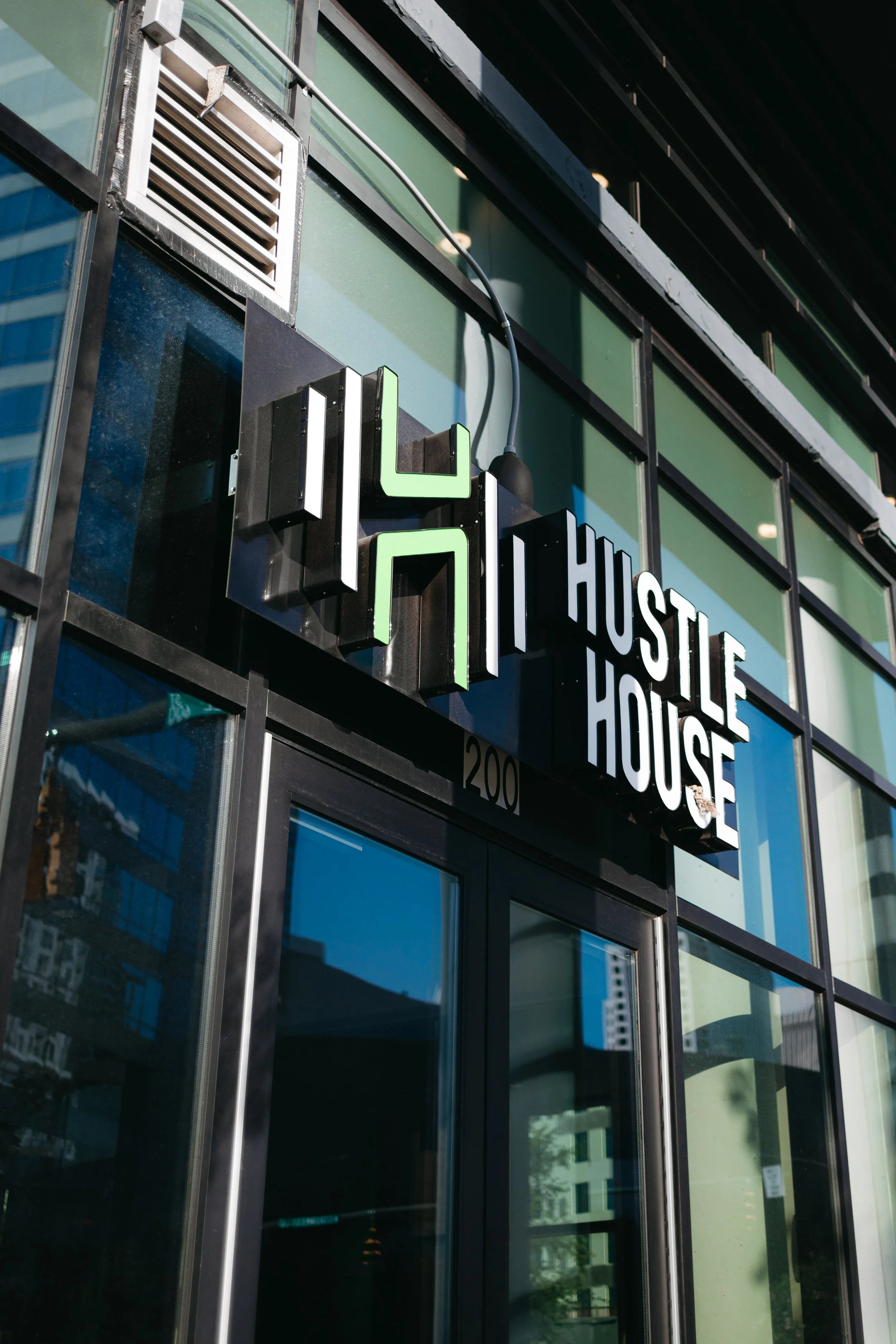 The exterior of a modern building with a black and white sign that reads "HUSTLE HOUSE" and features a stylized logo next to the sign.