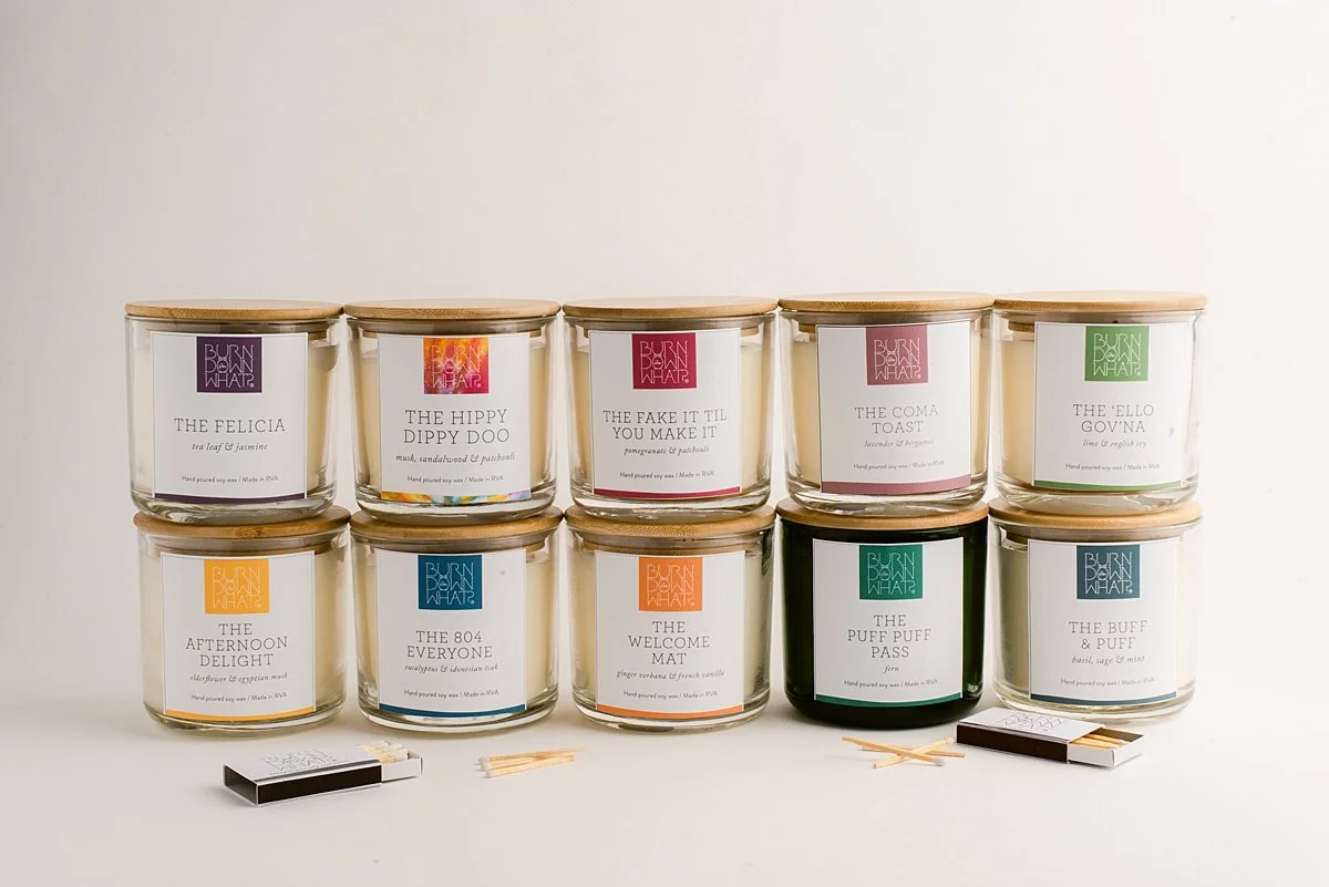 Ten candles with various labels and colors arranged in two rows on a white surface, with matches and lighter nearby.