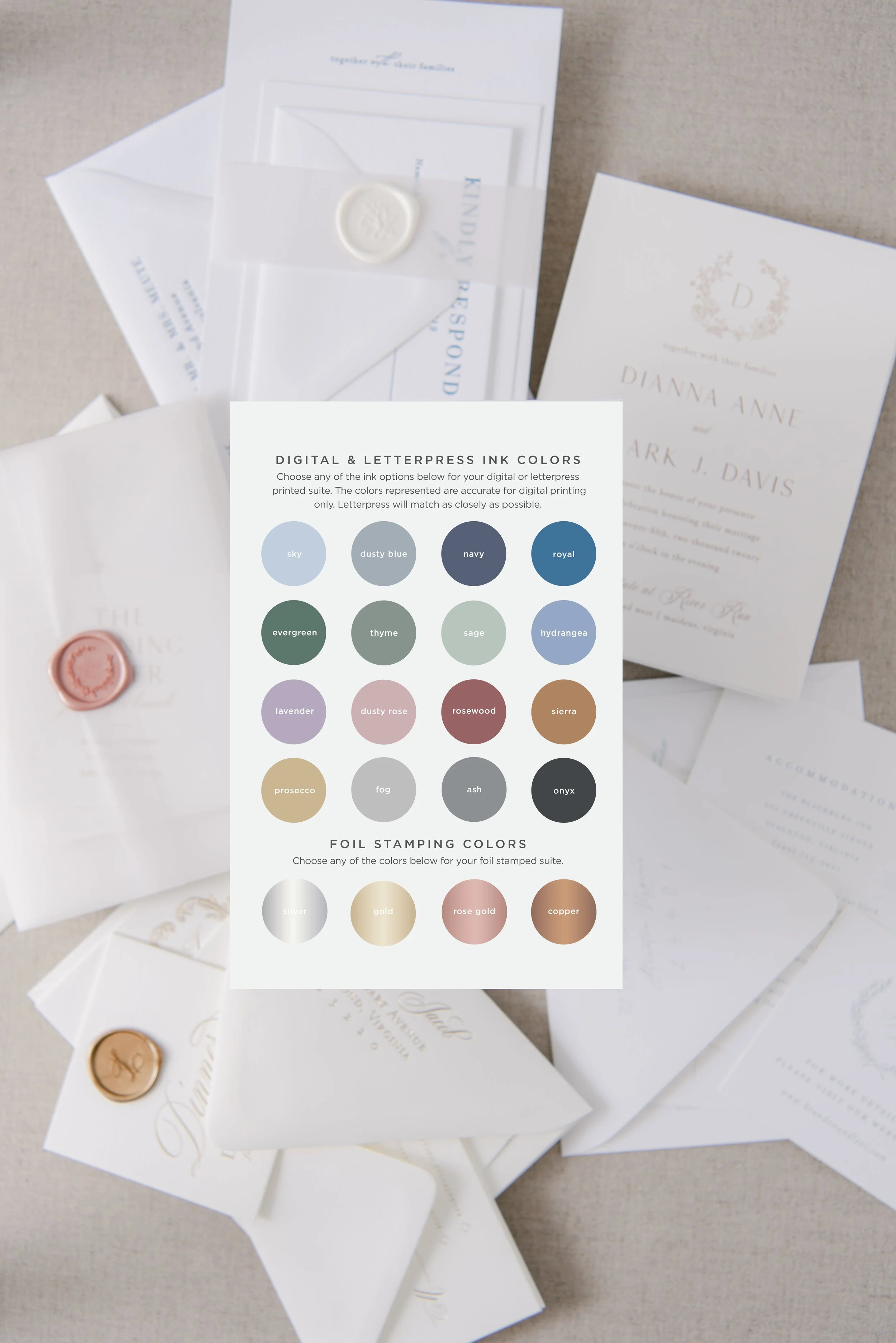 Invitation stationery with colored wax seals and a color selection chart for digital and foil stamp ink colors, set on a fabric surface.