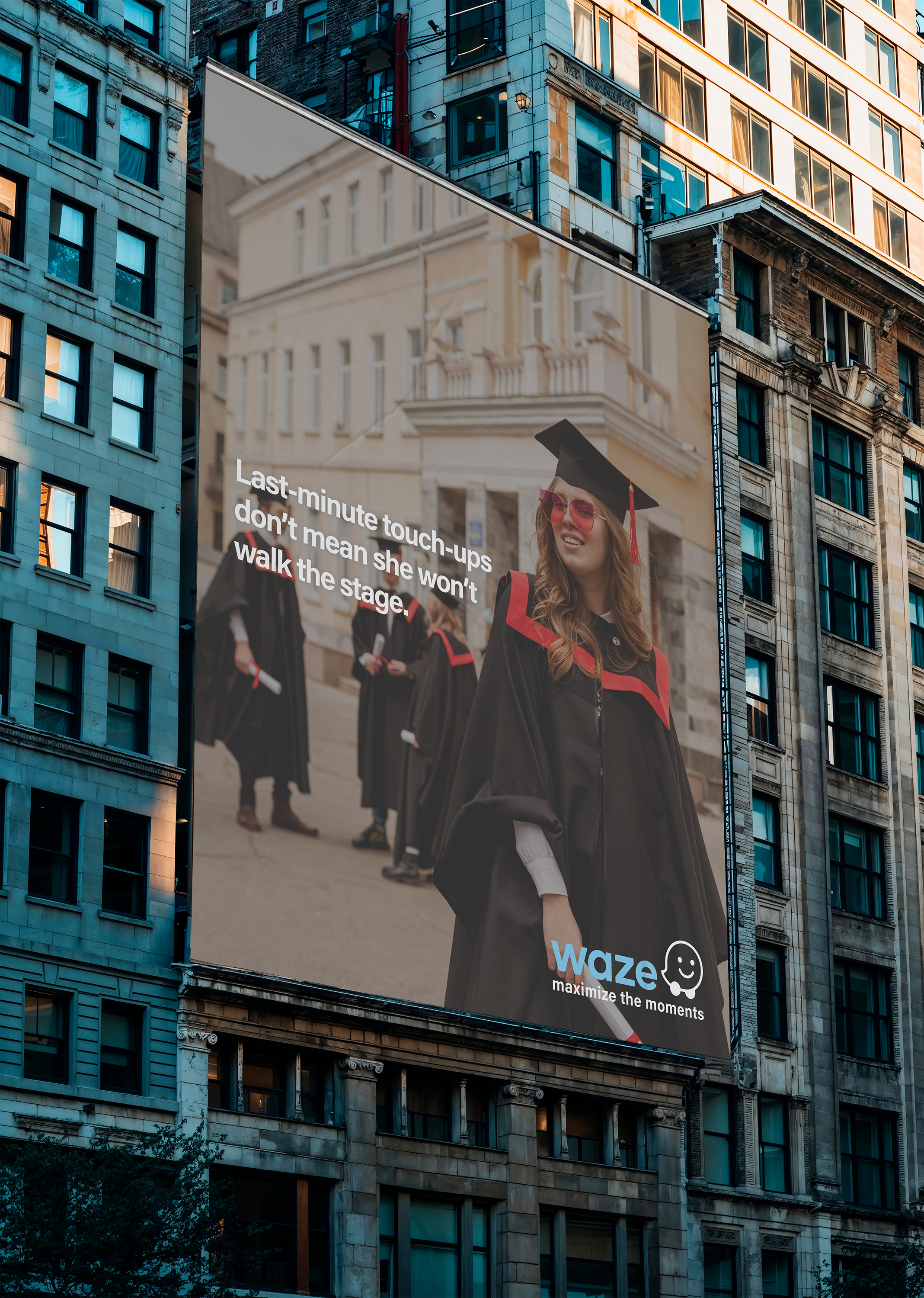 A large billboard on a city building features a woman wearing a graduation cap and sunglasses, smiling. The billboard advertises Waze with the slogan "maximize the moments" and a message about last-minute touch-ups.